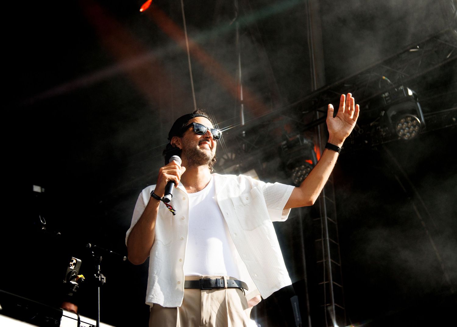 A performer in a white outfit sings passionately on stage with dramatic lighting and smoke effects in the background.