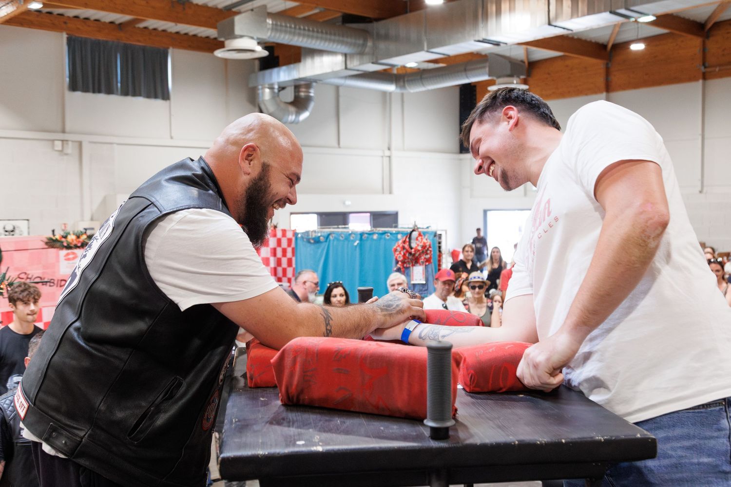 Two men competing in an arm wrestling match at a black table during an indoor sporting event.