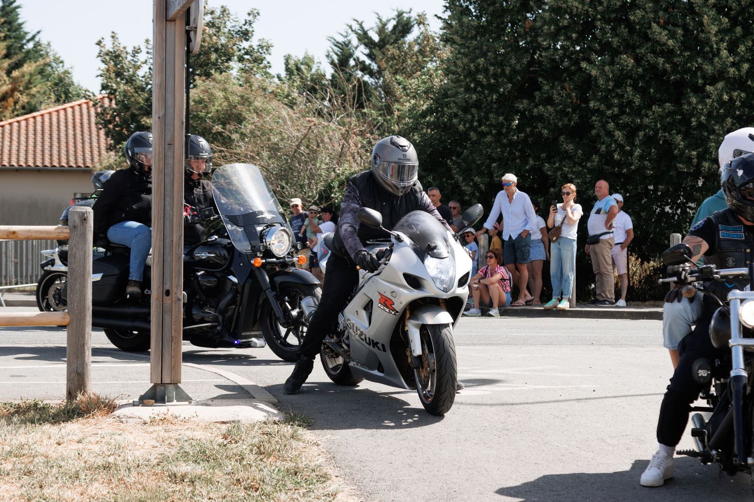 Motorcyclist in helmet riding white sport bike at outdoor gathering with spectators watching in background.
