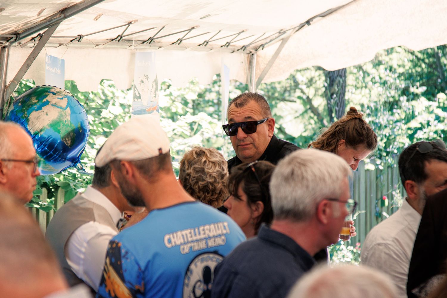 Wedding guests mingling under white tent canopy with globe balloon decoration at outdoor reception.