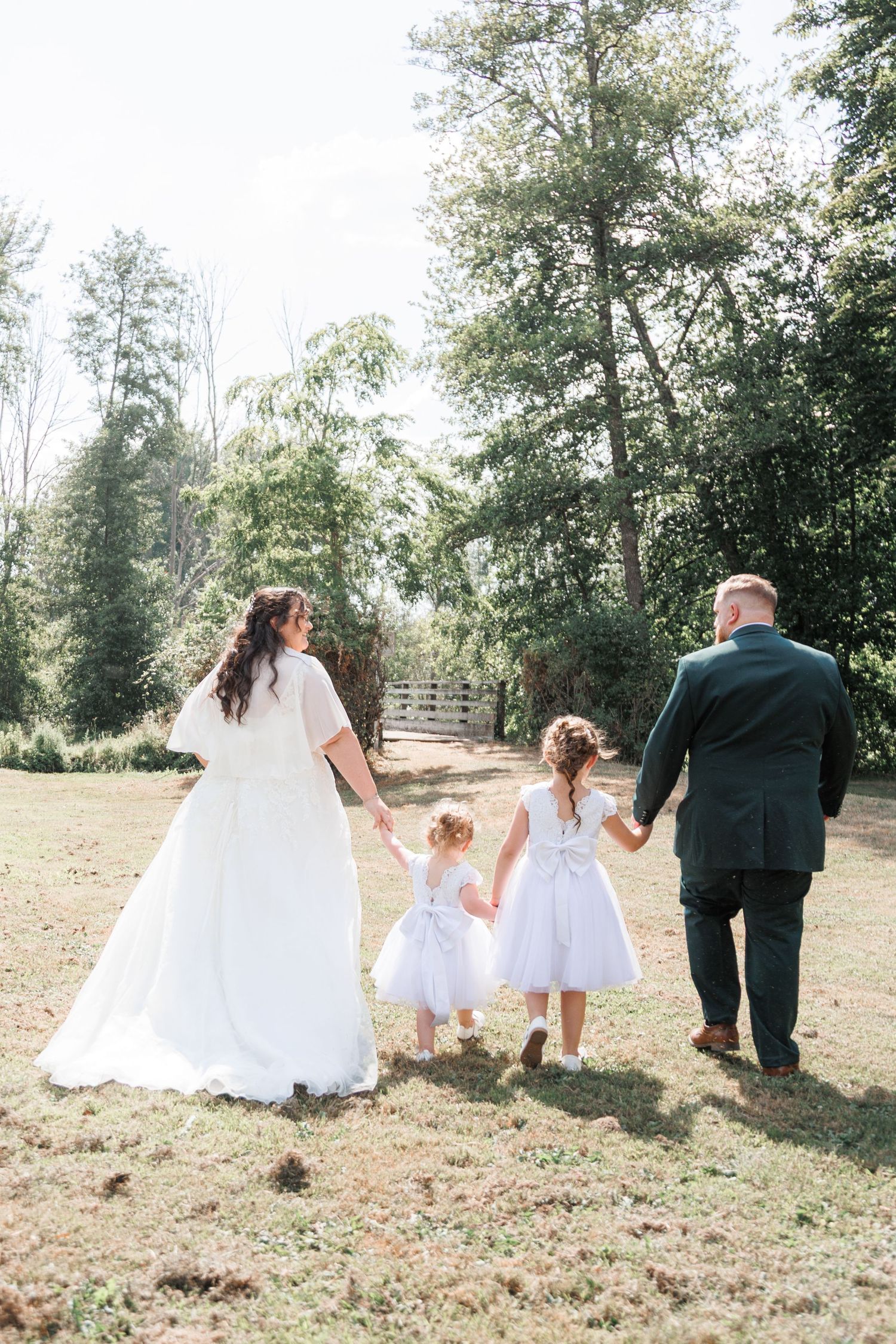 Bride and groom holding hands with two flower girls walking through a sunny outdoor garden.