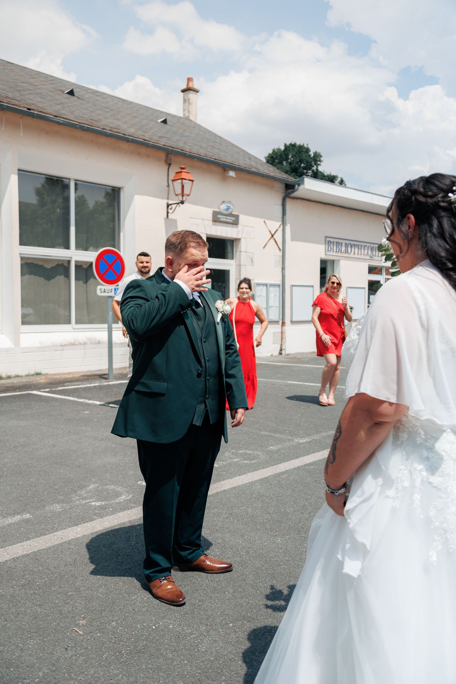 Emotional groom in dark green suit wipes tears seeing bride for first time on wedding day outdoors.
