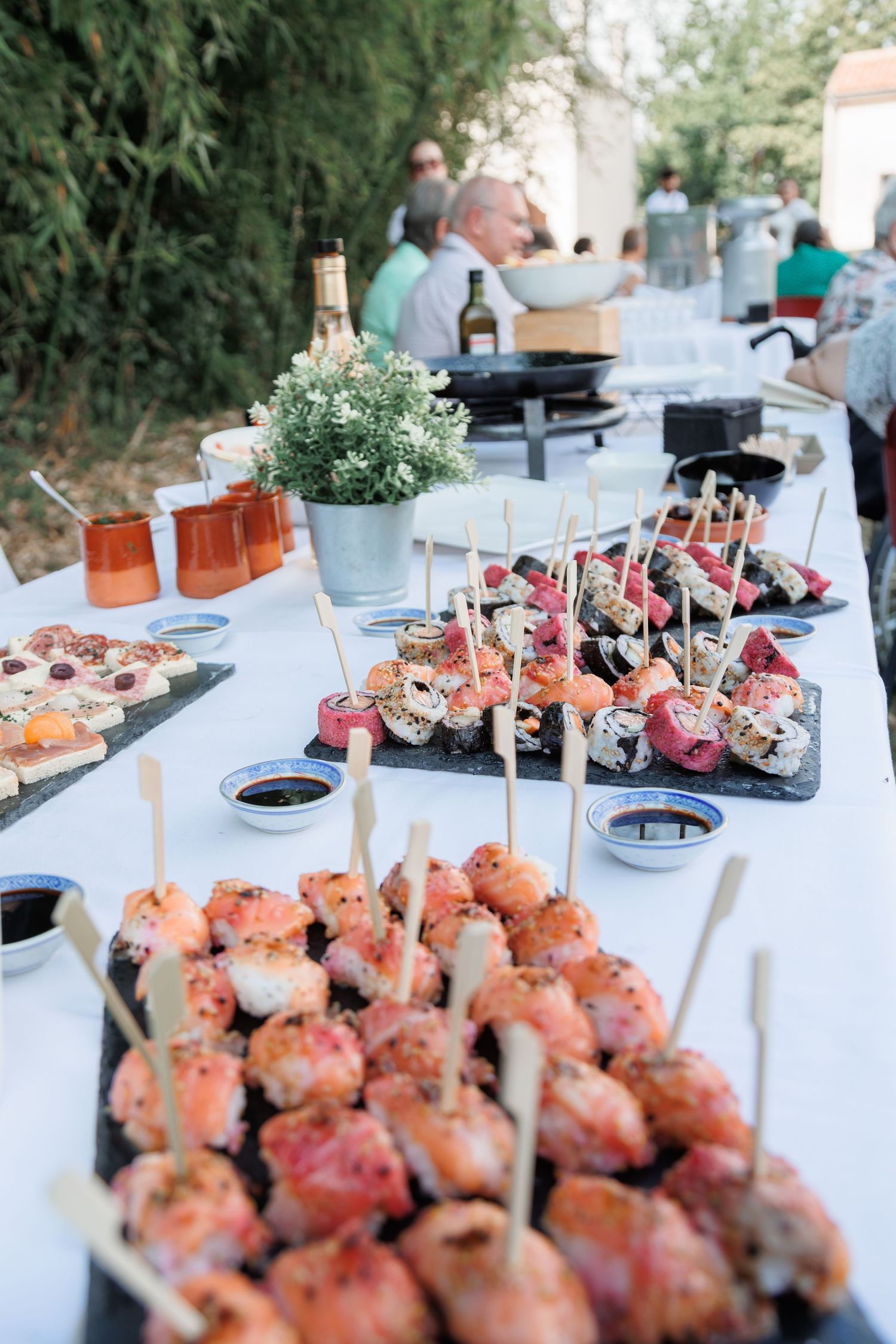 Elegant outdoor wedding reception buffet table with sushi appetizers and assorted finger foods.