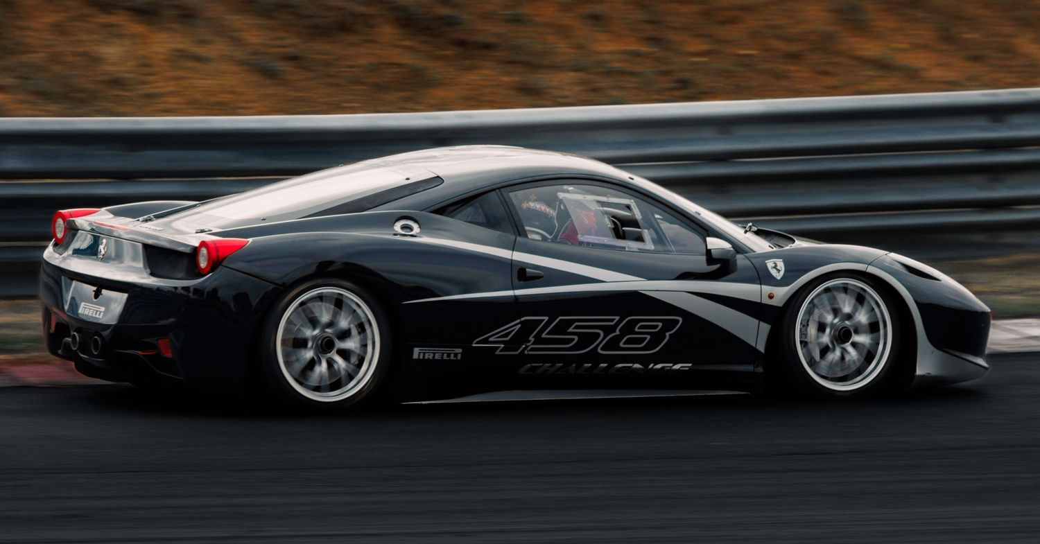 A black Ferrari 458 race car with white wheels drives on a race track during competition.