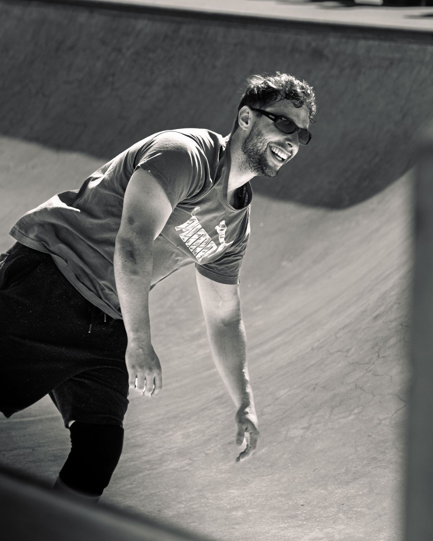 Black and white portrait of athlete smiling on curved ramp at skate park.