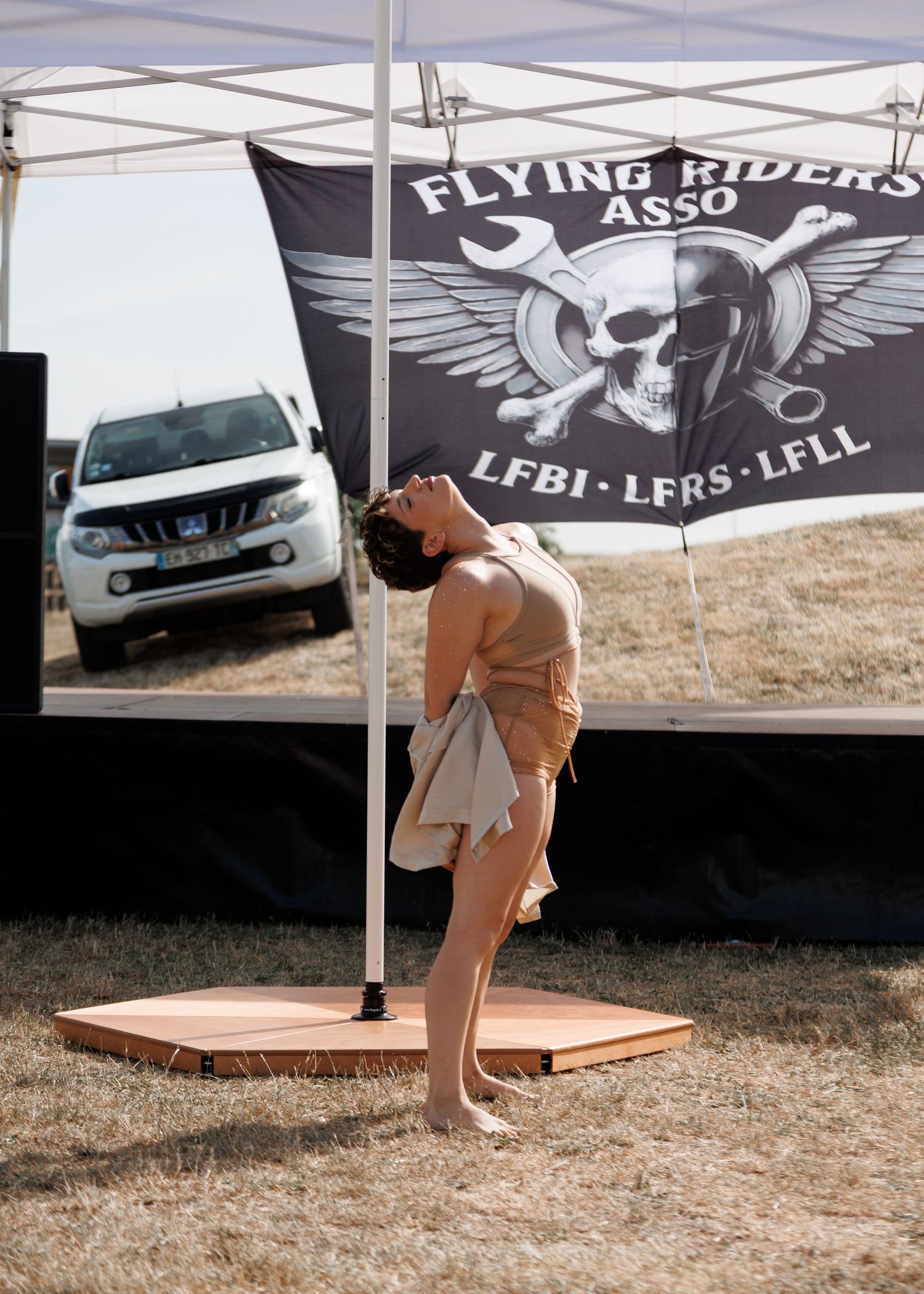 A dancer performs under a Flying Riders Association banner at an outdoor aviation event on a wooden stage.