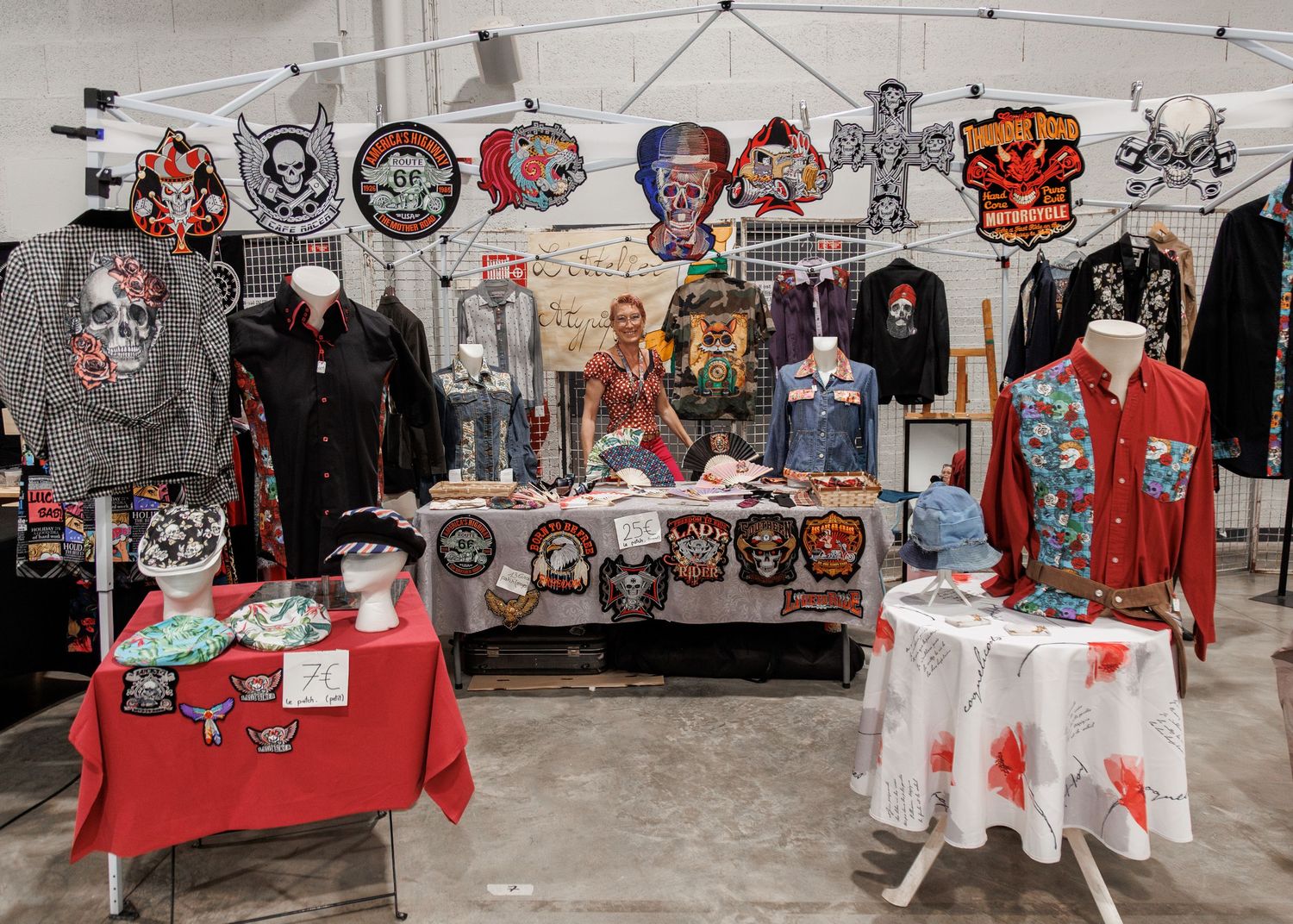 Vendor booth displaying rock-themed patches, embroidered jackets, and apparel on mannequins at an indoor market.