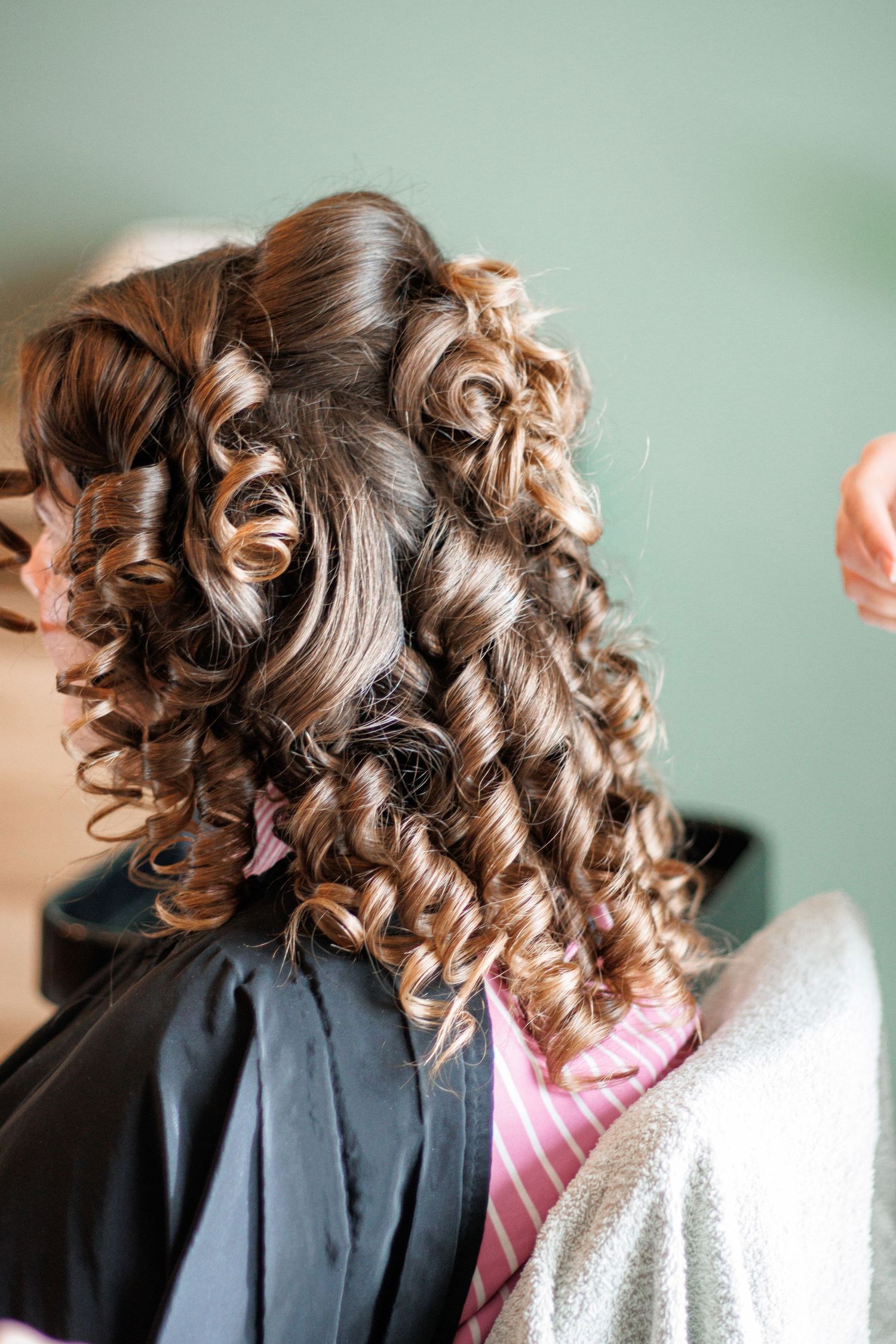 Back view of a woman with elegant curly brown hair styled in ringlets during a bridal hair preparation session.