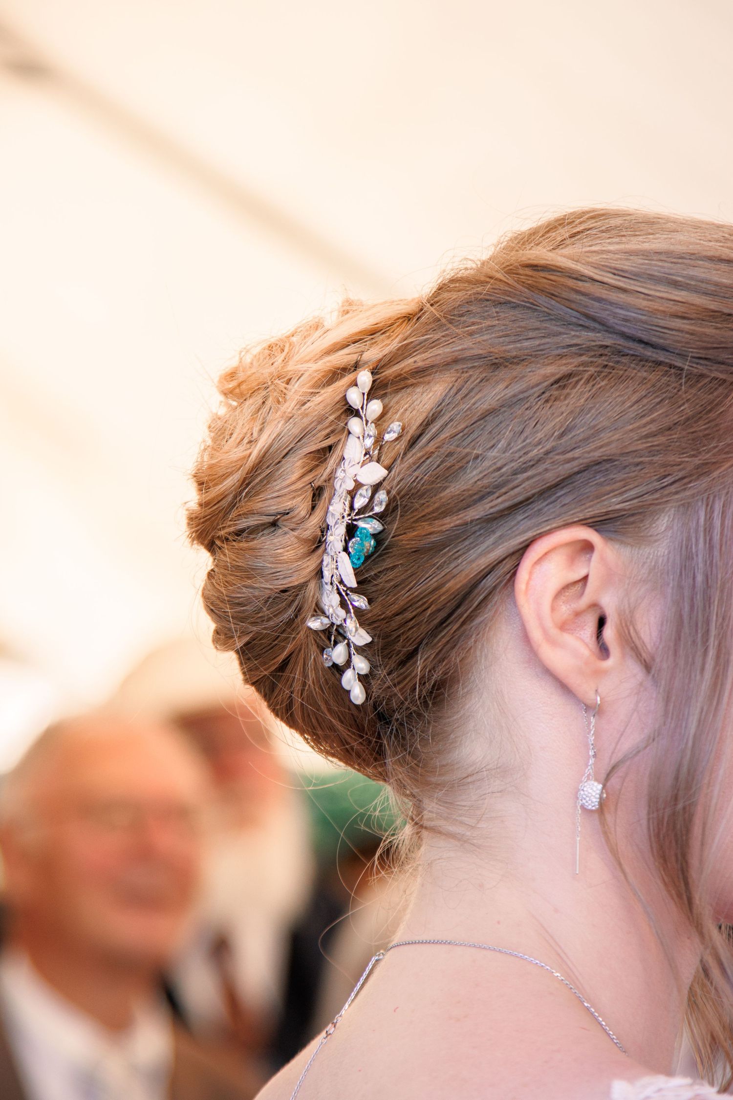 Close-up of bride's elegant updo hairstyle adorned with pearl and turquoise hair accessory at wedding.