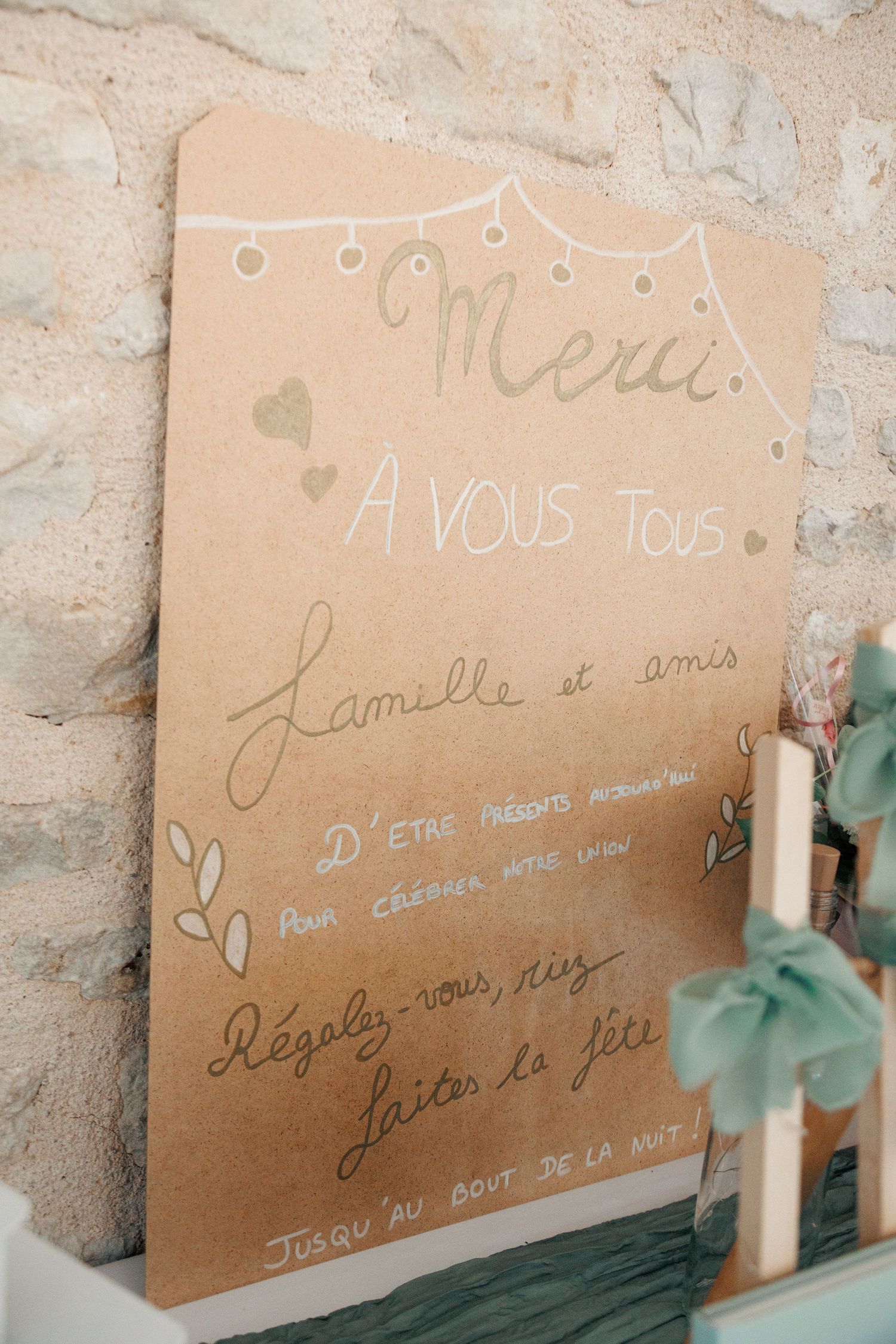 Handwritten French wedding thank you sign on kraft paper leaning against a stone wall.