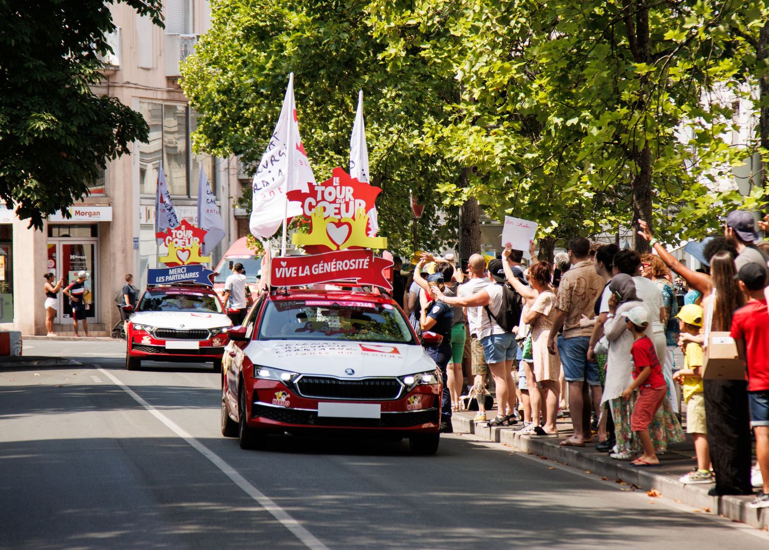 Decorated promotional vehicles drive down a street lined with cheering spectators during a parade.