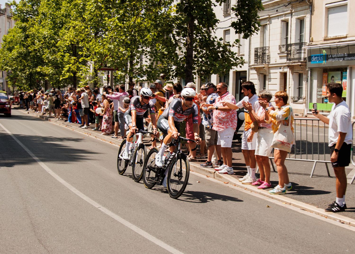 Cyclists racing along a road lined with spectators during a summer event.