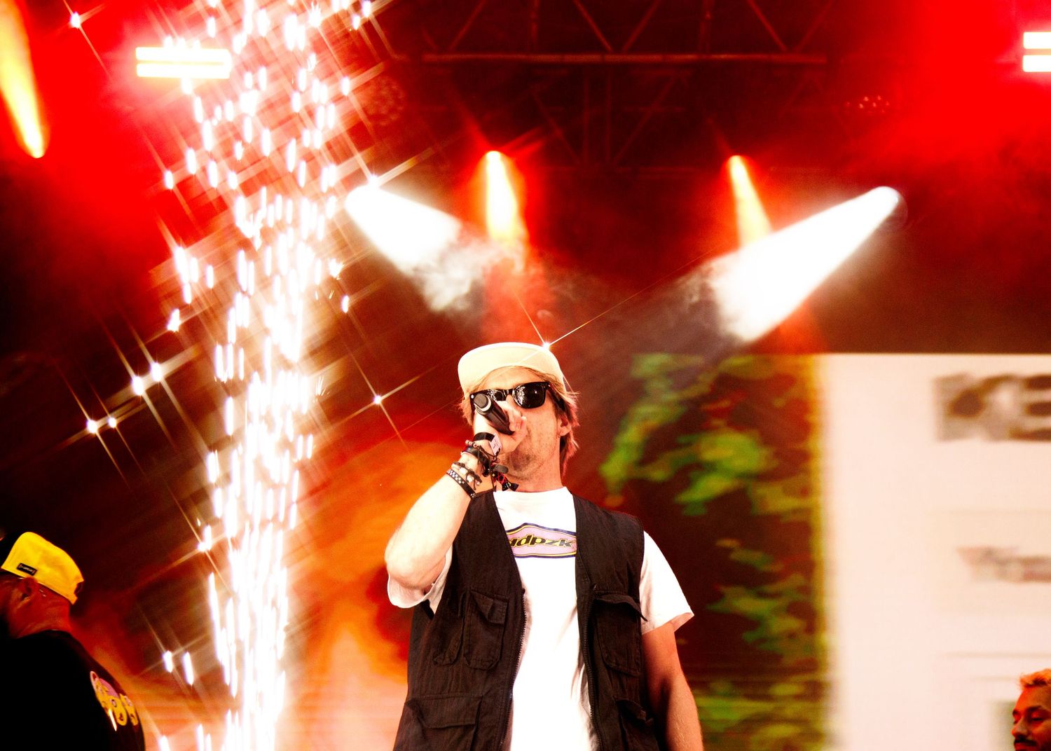 A performer on stage with red lighting effects and sparks flying in the background during a concert performance.