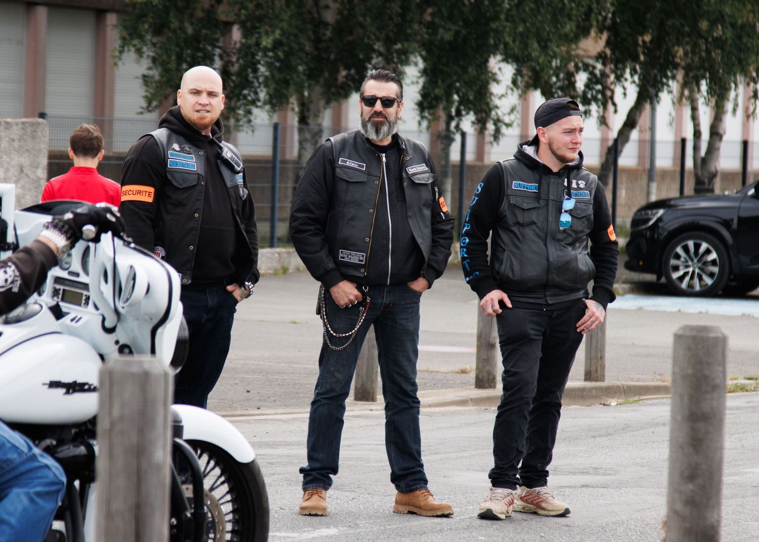 Three bikers in leather jackets standing near parked motorcycles.