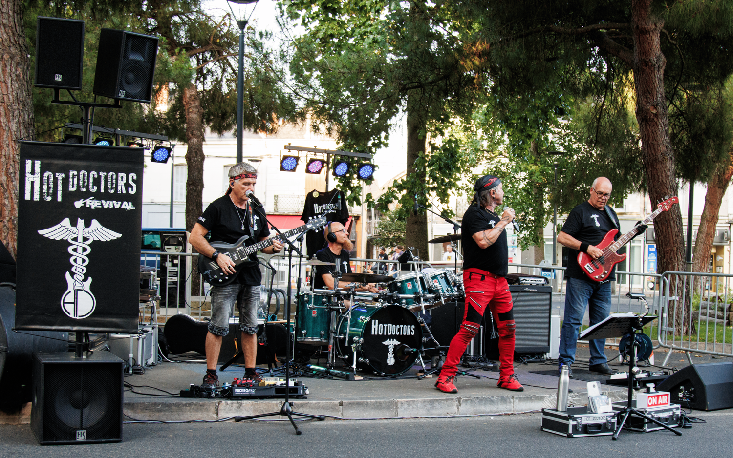Rock band performing on outdoor stage with instruments and equipment set up.