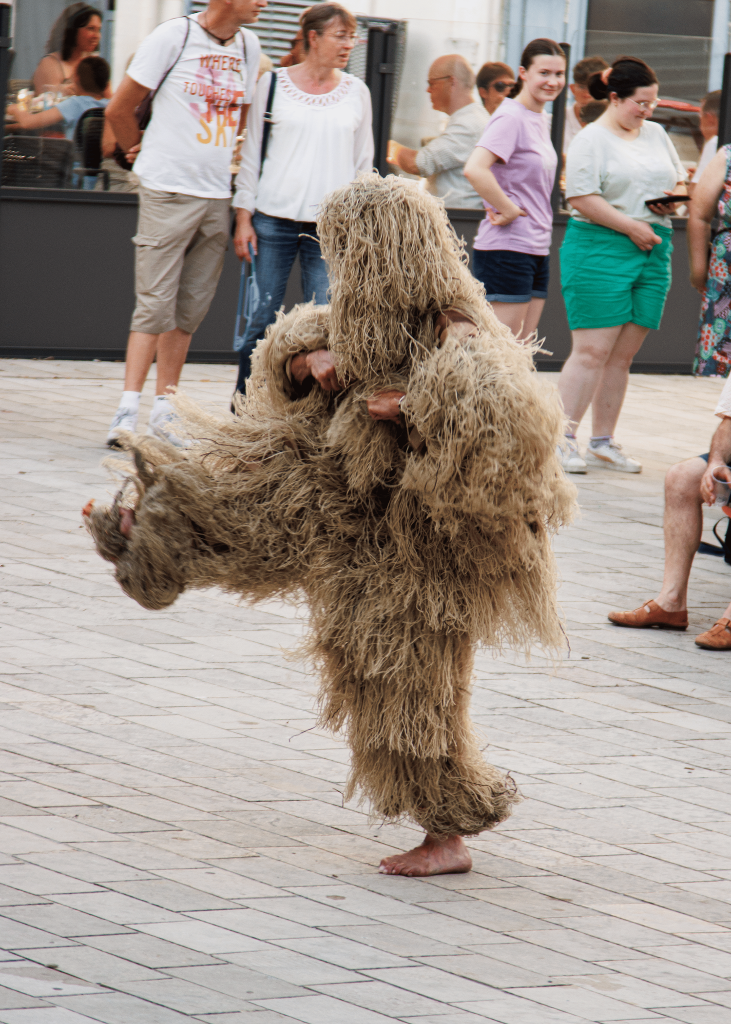 A person in a furry mascot costume dances on a plaza while spectators watch.