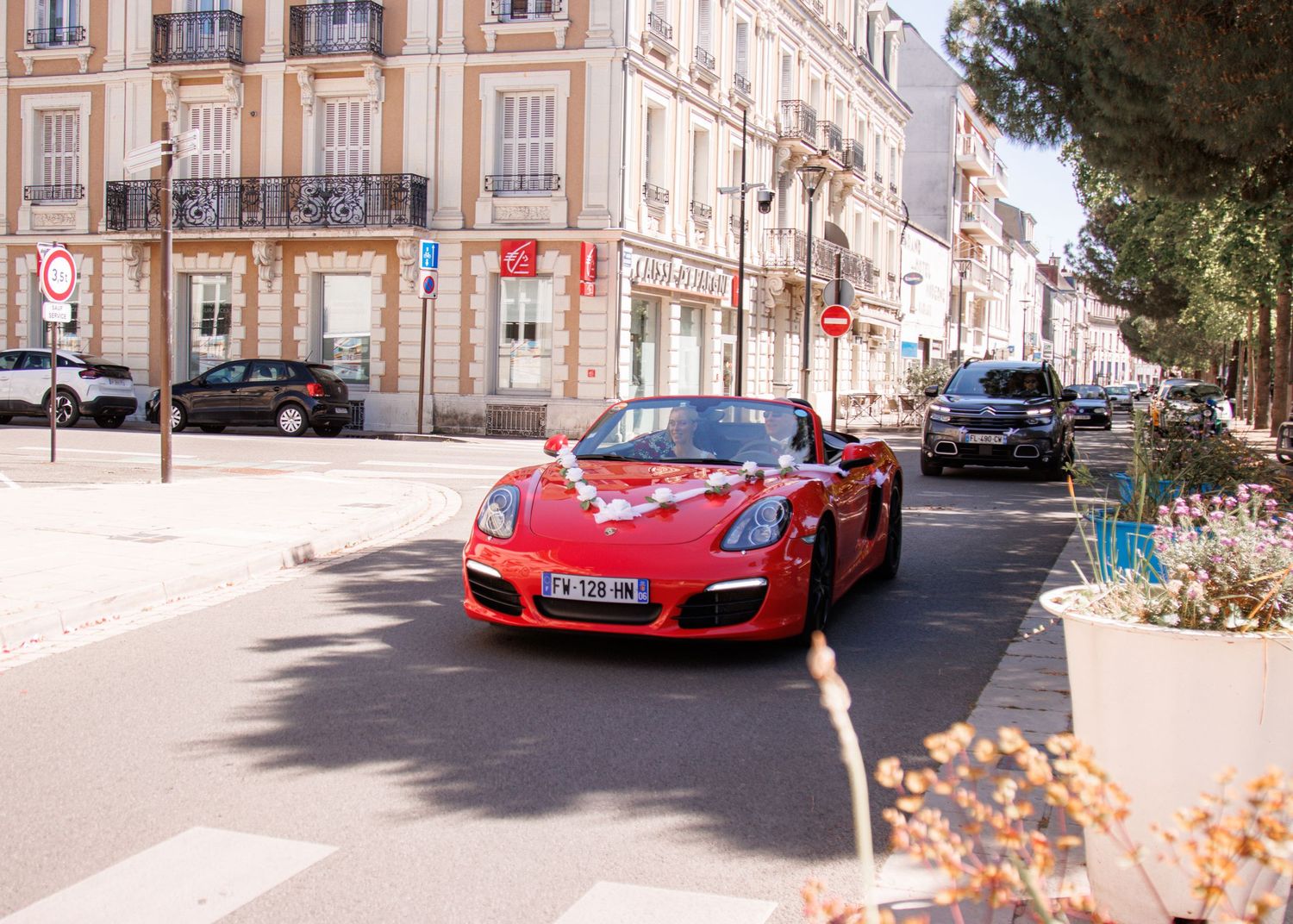 Red Porsche Boxster convertible decorated for wedding drives through sunny French street.