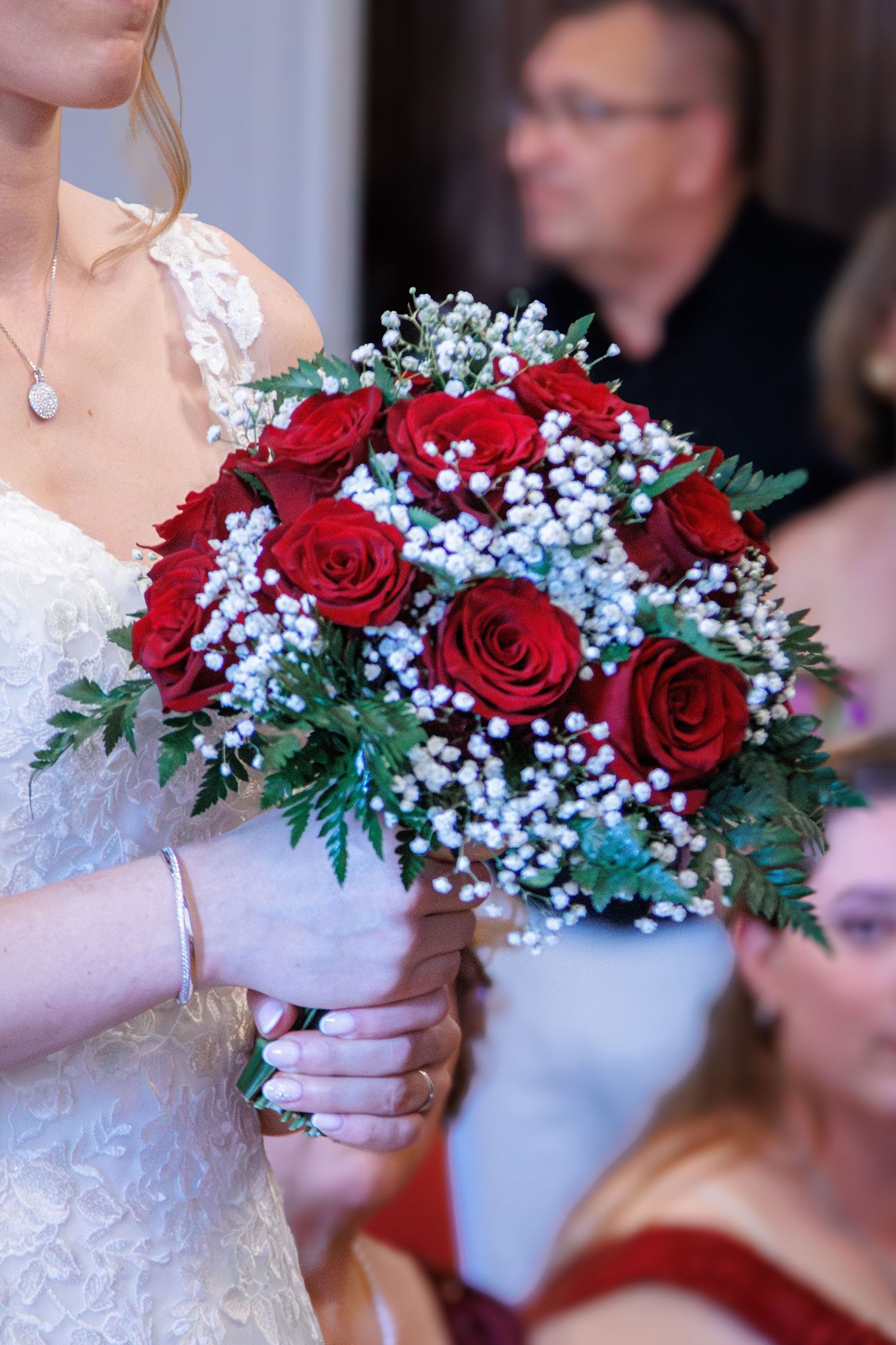 Bride holding stunning red rose bouquet with white baby's breath at wedding ceremony.