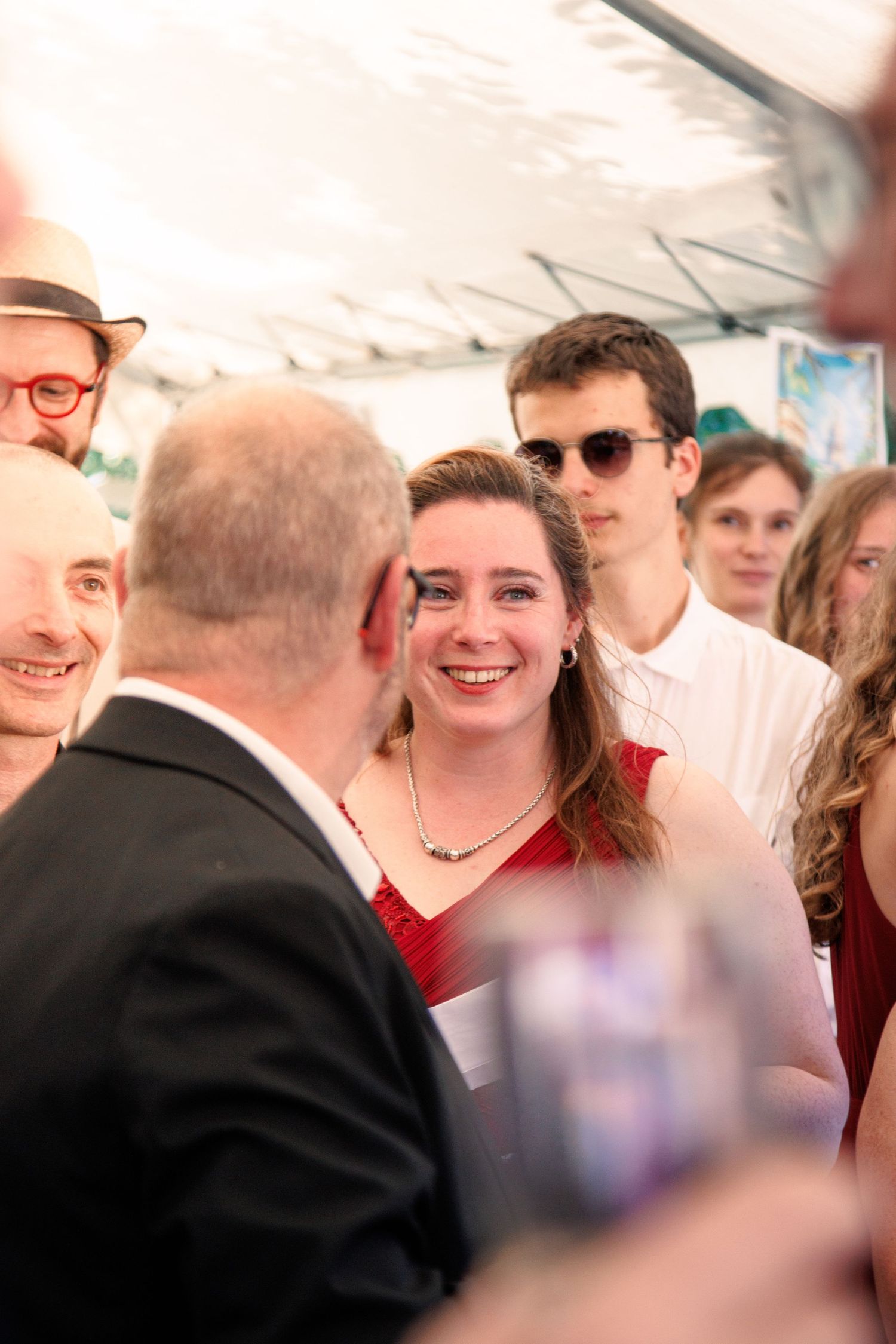 Smiling woman in red dress mingles with wedding guests under a tent at a festive reception.