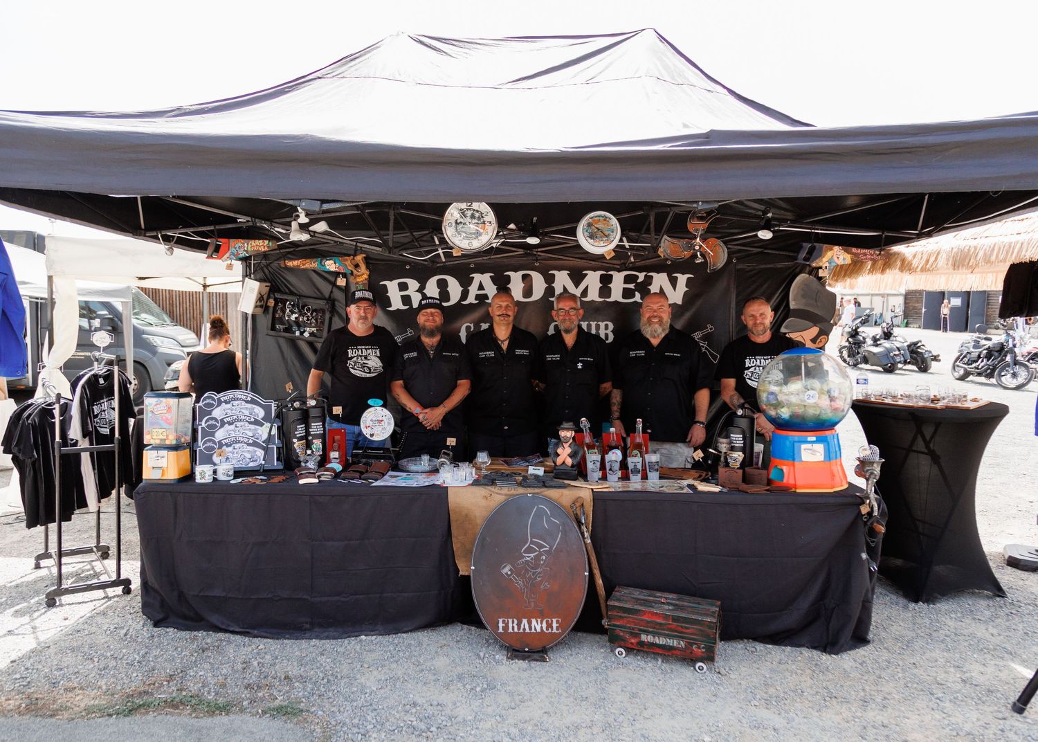 Roadmen club booth with members standing behind a merchandise table under a black canopy at an outdoor event.