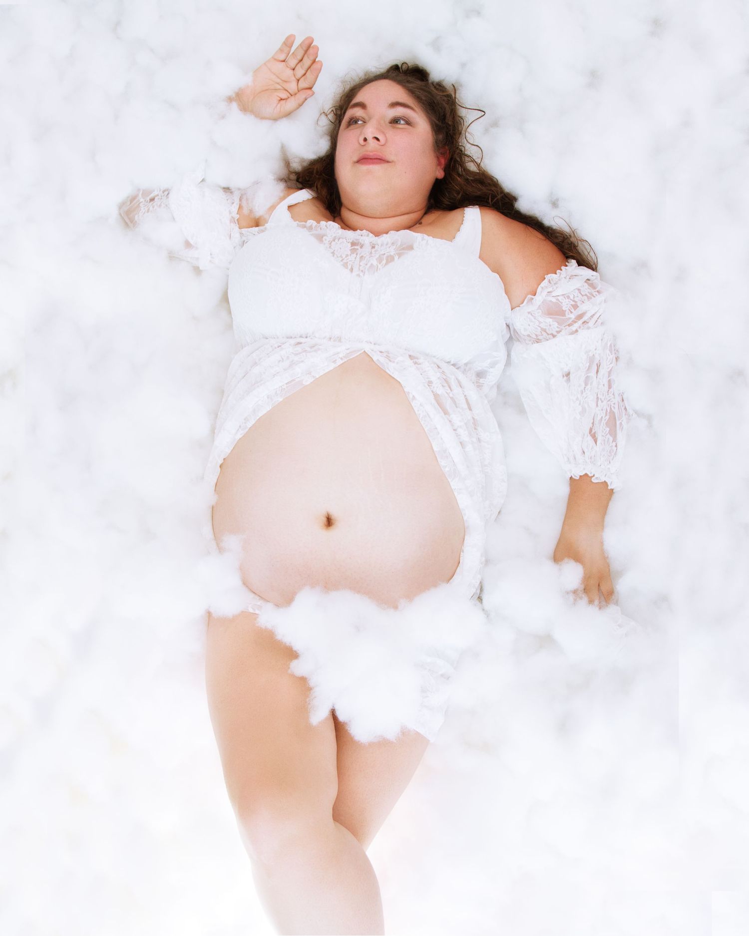 Artistic maternity portrait with dreamy white fabric and lace details.