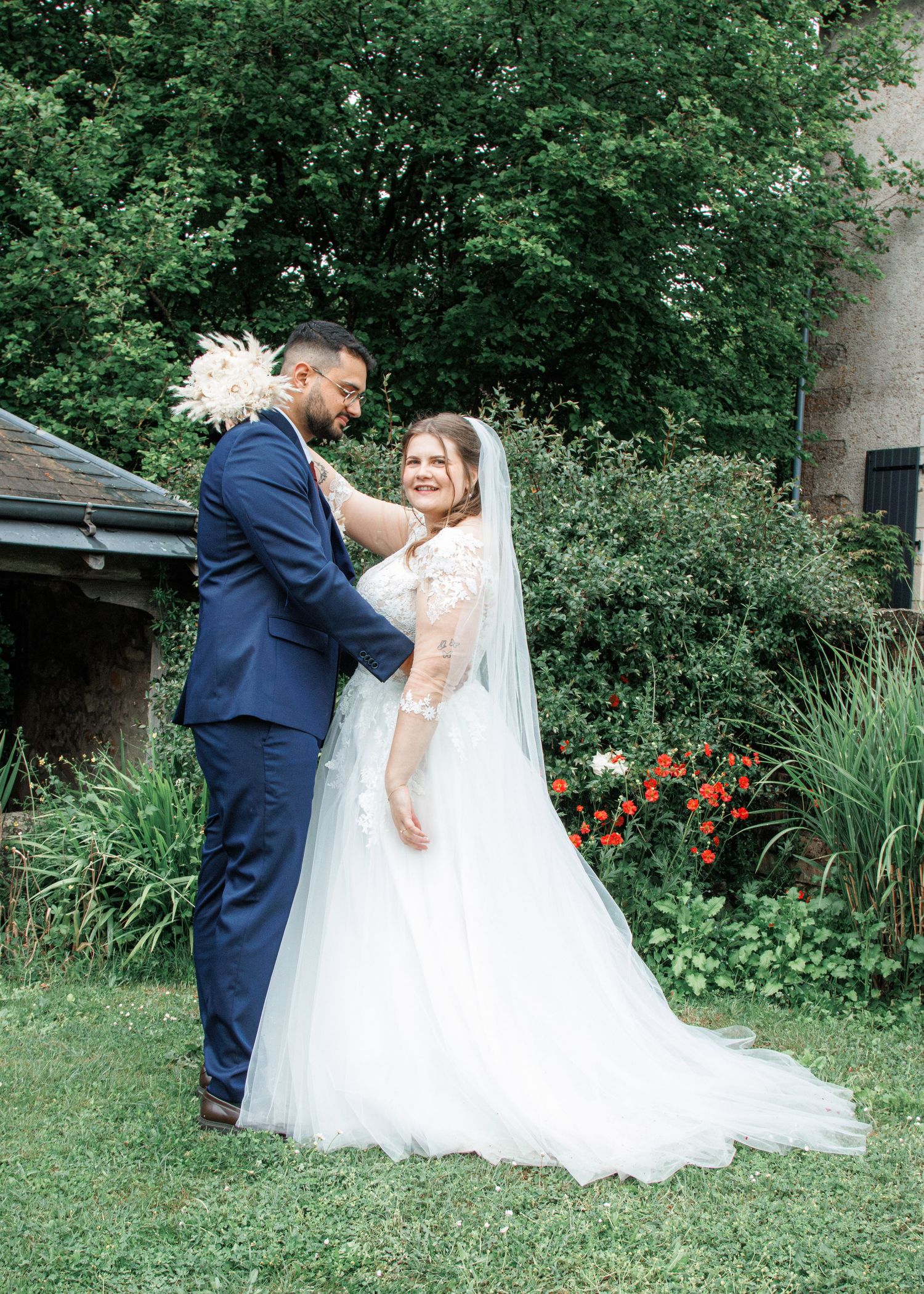 A bride and groom share a tender moment outdoors, with the bride in a white tulle gown and veil, groom in a navy suit.