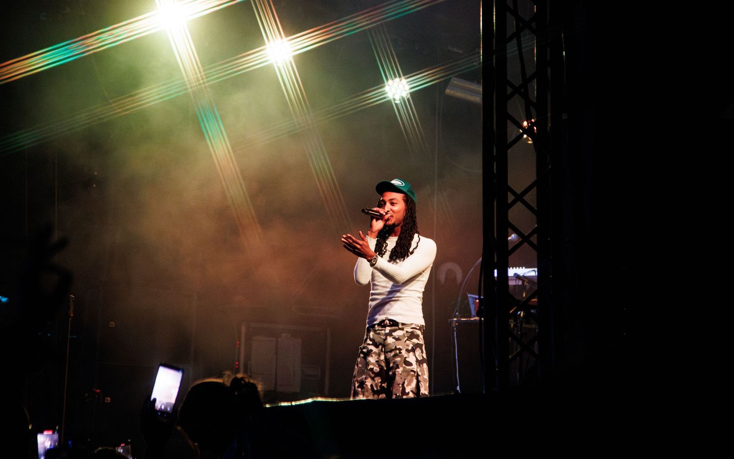 Singer performing on stage under bright lights with smoke effects at an outdoor concert at night.