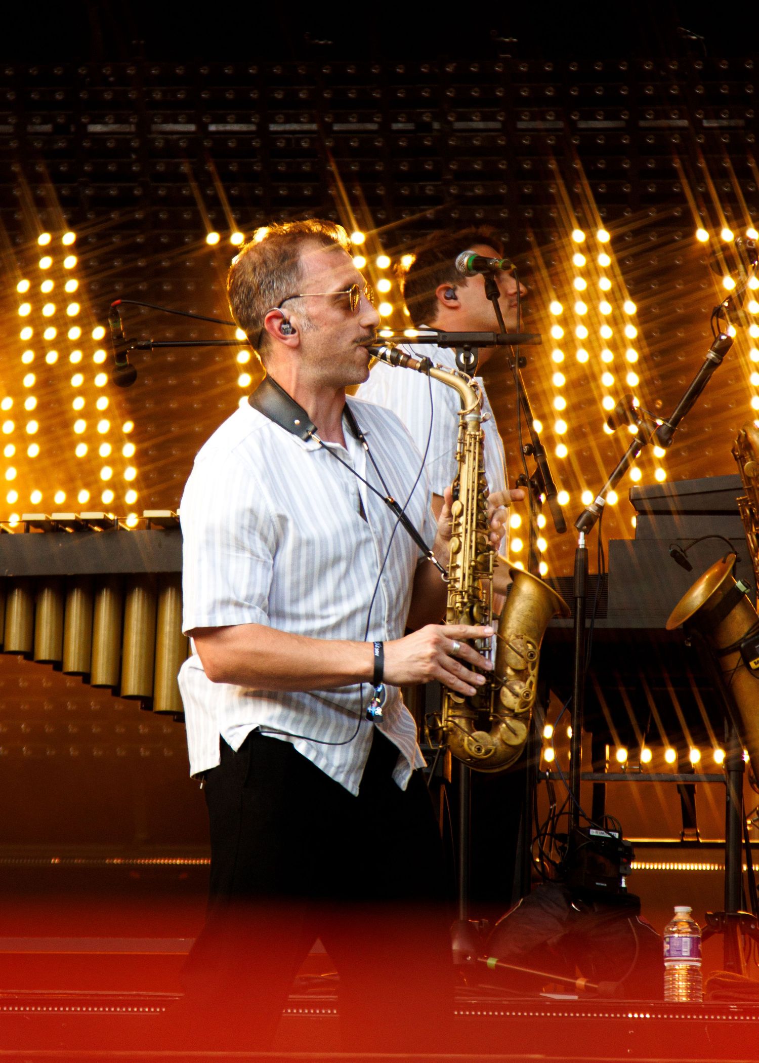 Musician playing alto saxophone on a bright concert stage with glowing yellow lights in the background.