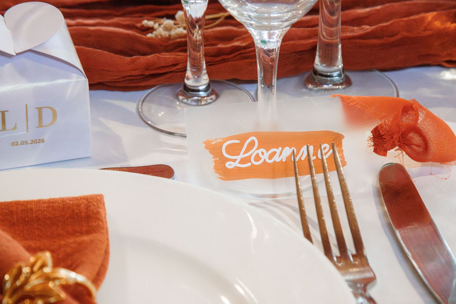 Elegant wedding table setting with orange napkins, crystal glasses, and a personalized name card place setting.