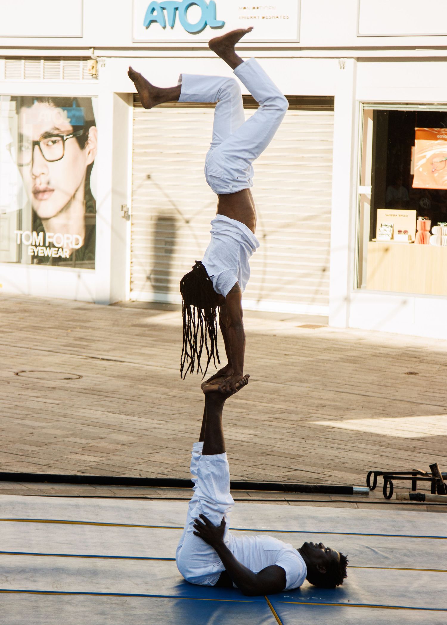 Two street performers execute an impressive inverted acrobatic balance pose outside a storefront.