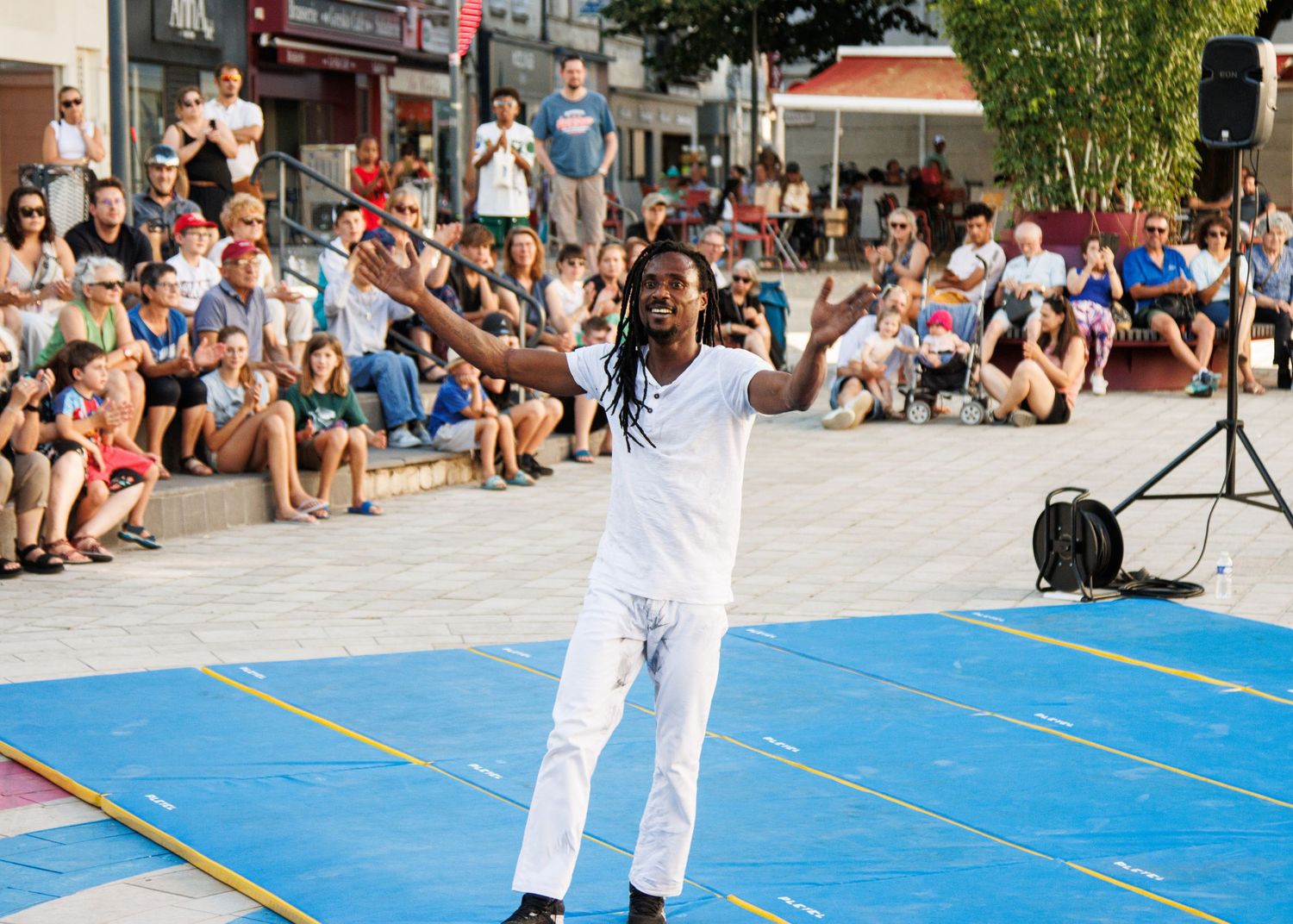 Performer in white attire energetically gestures to a crowd during a street performance.