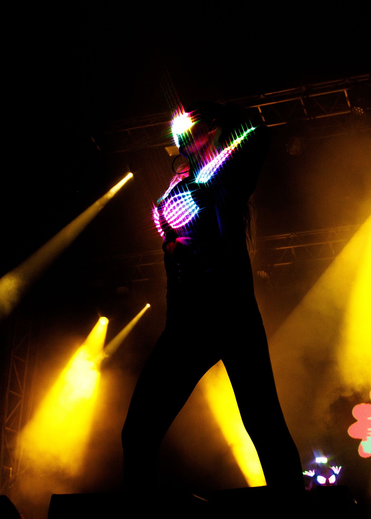 A silhouetted performer on stage dancing with colorful LED lights and yellow spotlights creating a dramatic effect.