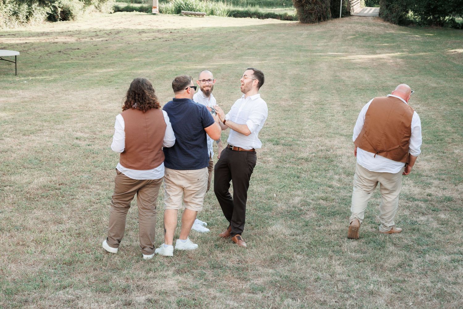 Group of men chatting casually on green lawn during outdoor wedding reception.