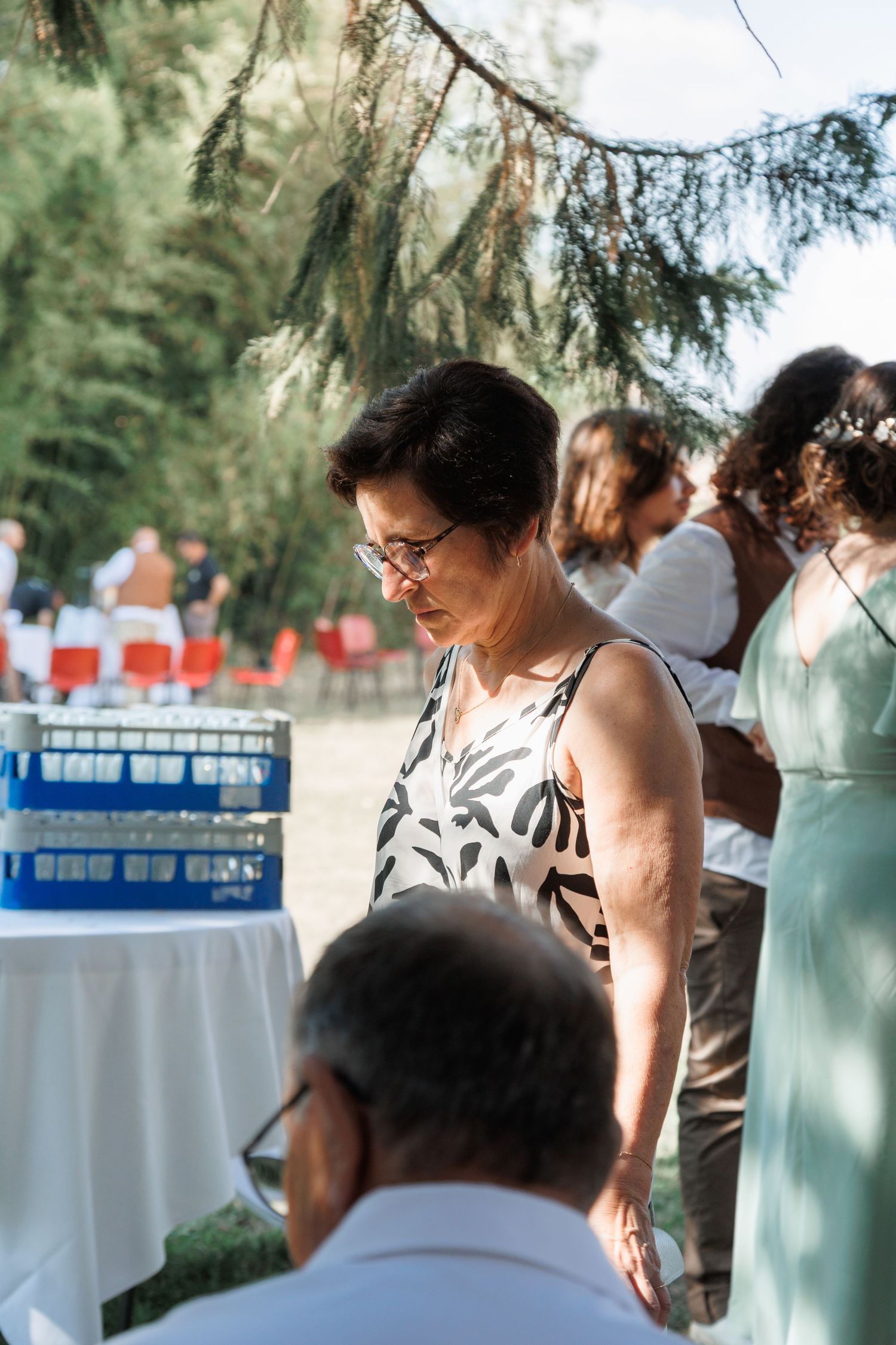 Older woman with glasses in floral dress at an outdoor wedding reception event.