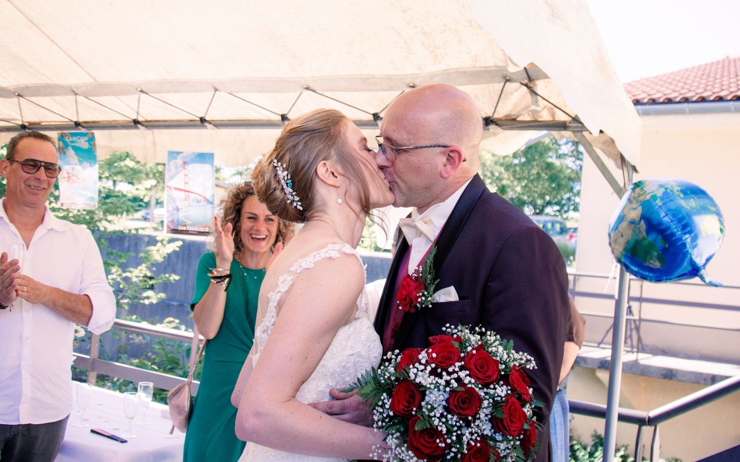 Bride and groom share first kiss under white tent at outdoor wedding ceremony.