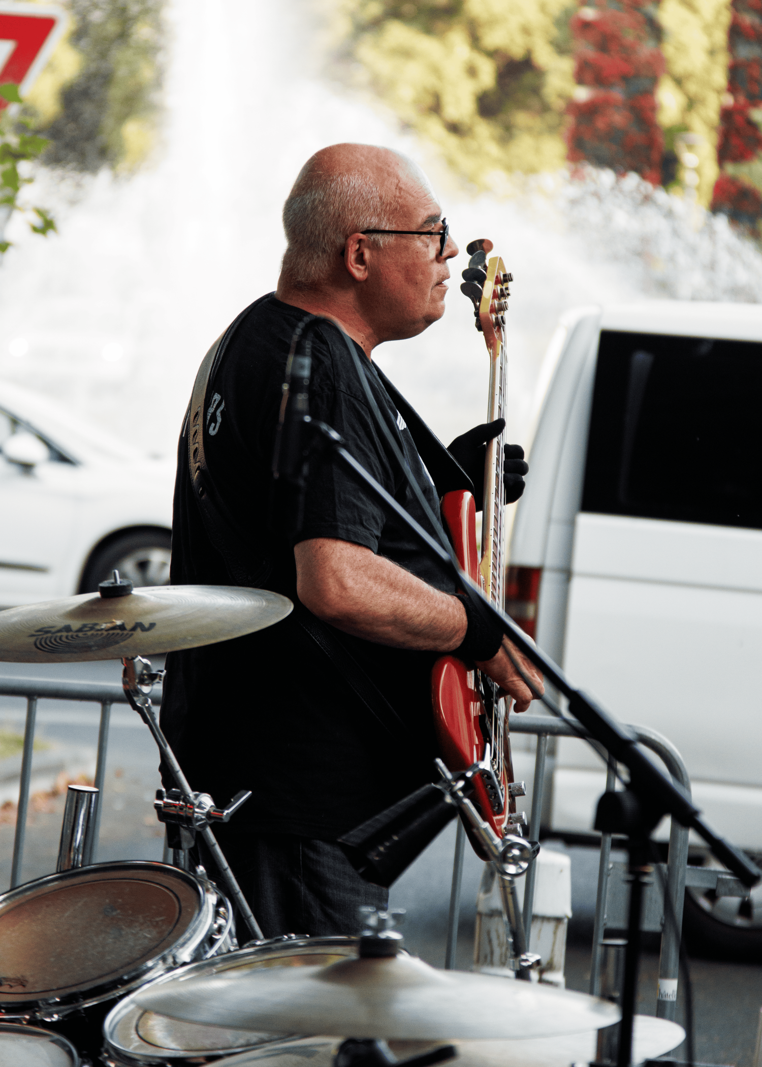 Musician performing with a microphone next to drum kit at outdoor concert.