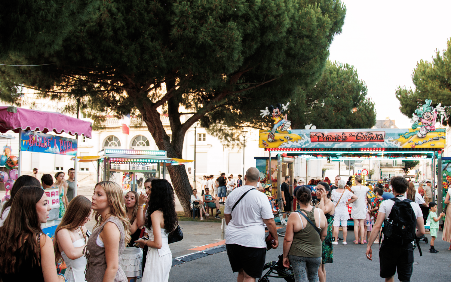 Outdoor festival scene with trees and carnival rides in the background at dusk.