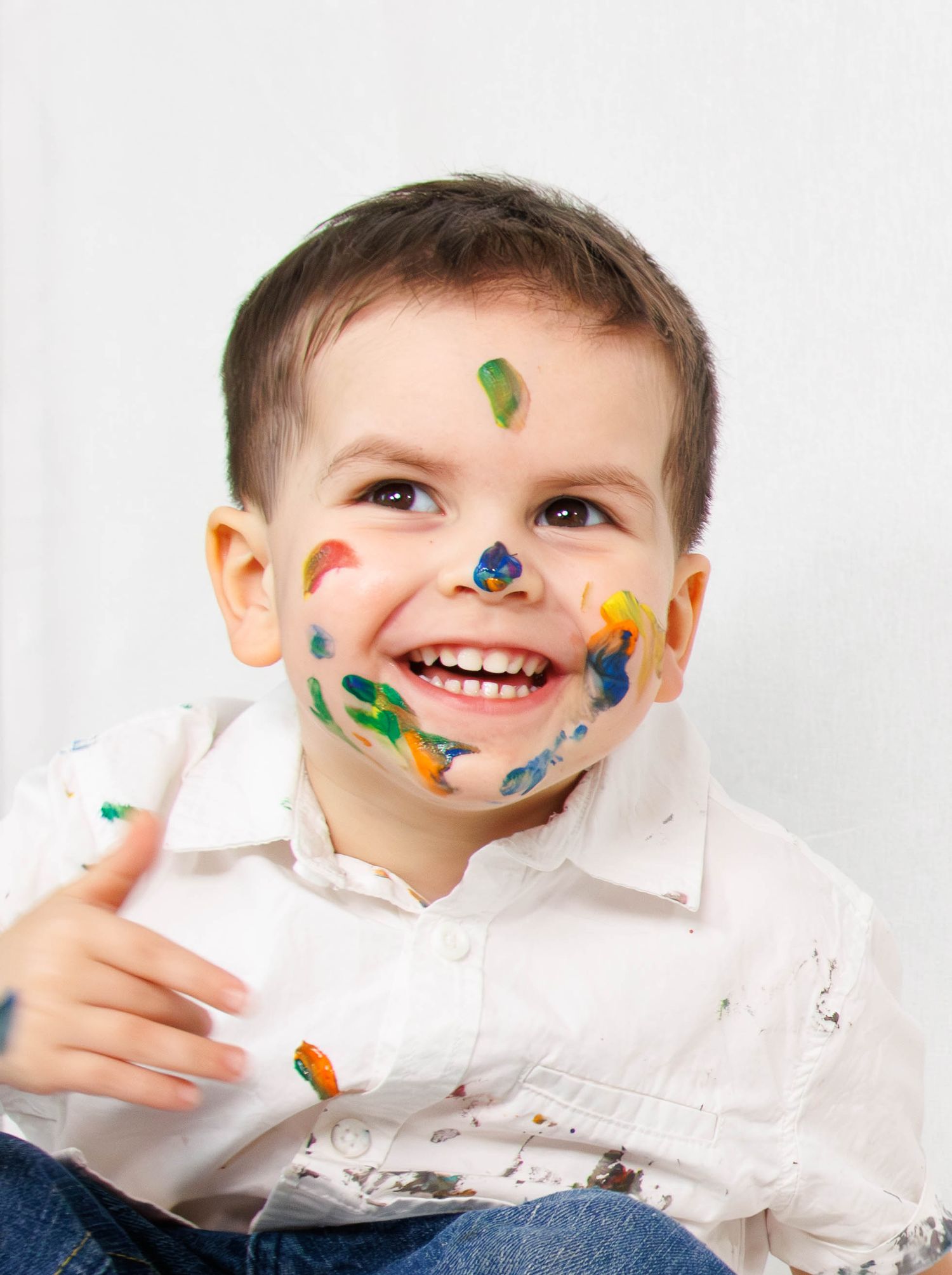Child wearing white shirt with colorful paint marks on face during art activity.