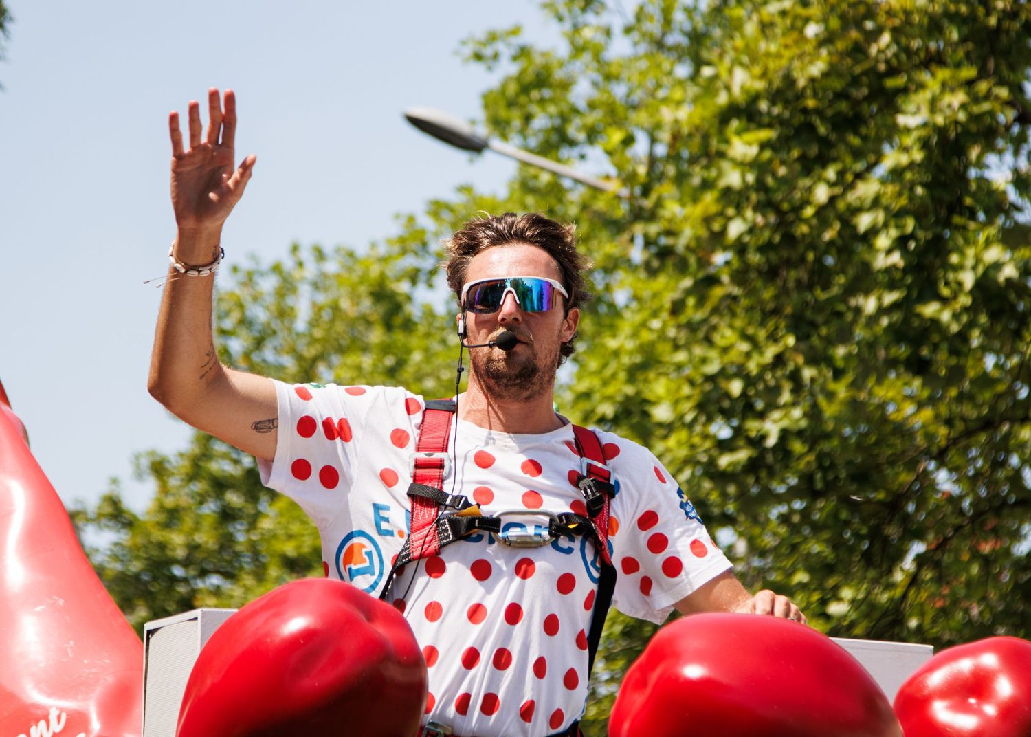 Participant in polka dot jersey waving to crowd during cycling event parade.