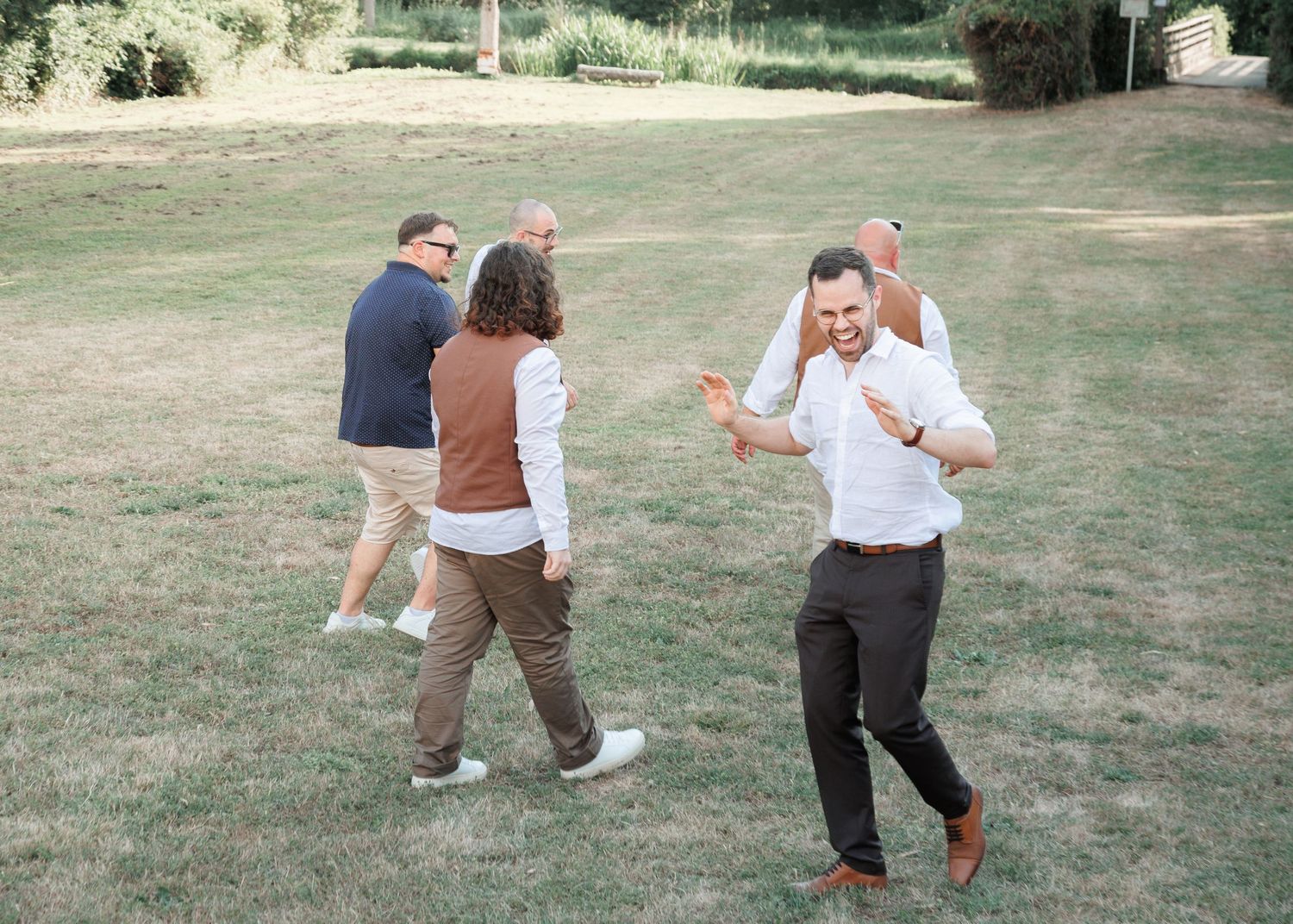 Wedding guests laughing and dancing together on a green lawn during outdoor celebrations.