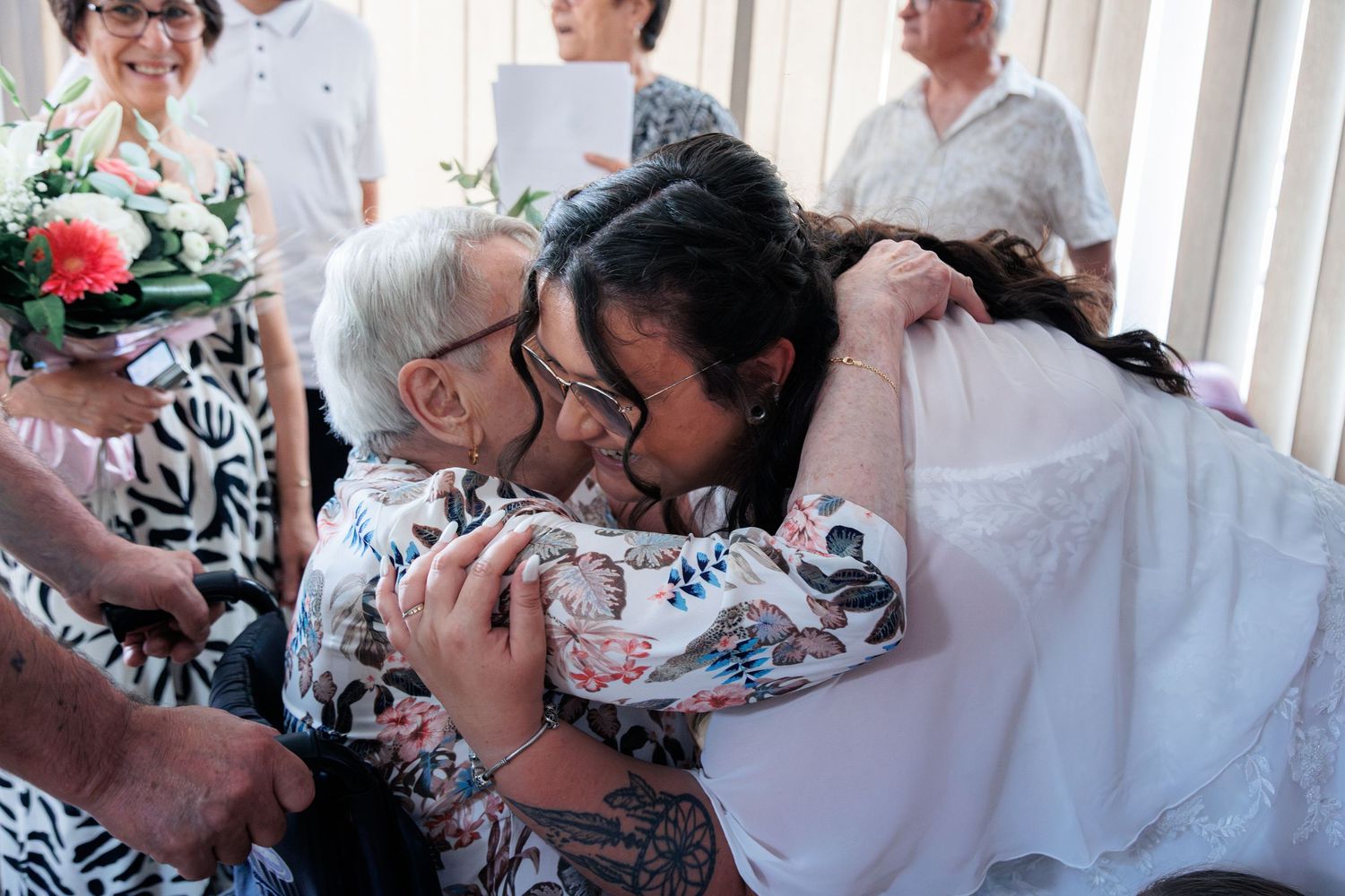 Bride in white wedding dress warmly embraces elderly guest after wedding ceremony celebration.