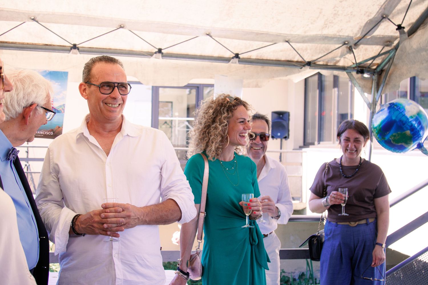 Guests laughing and socializing under a tent at an outdoor wedding reception celebration.
