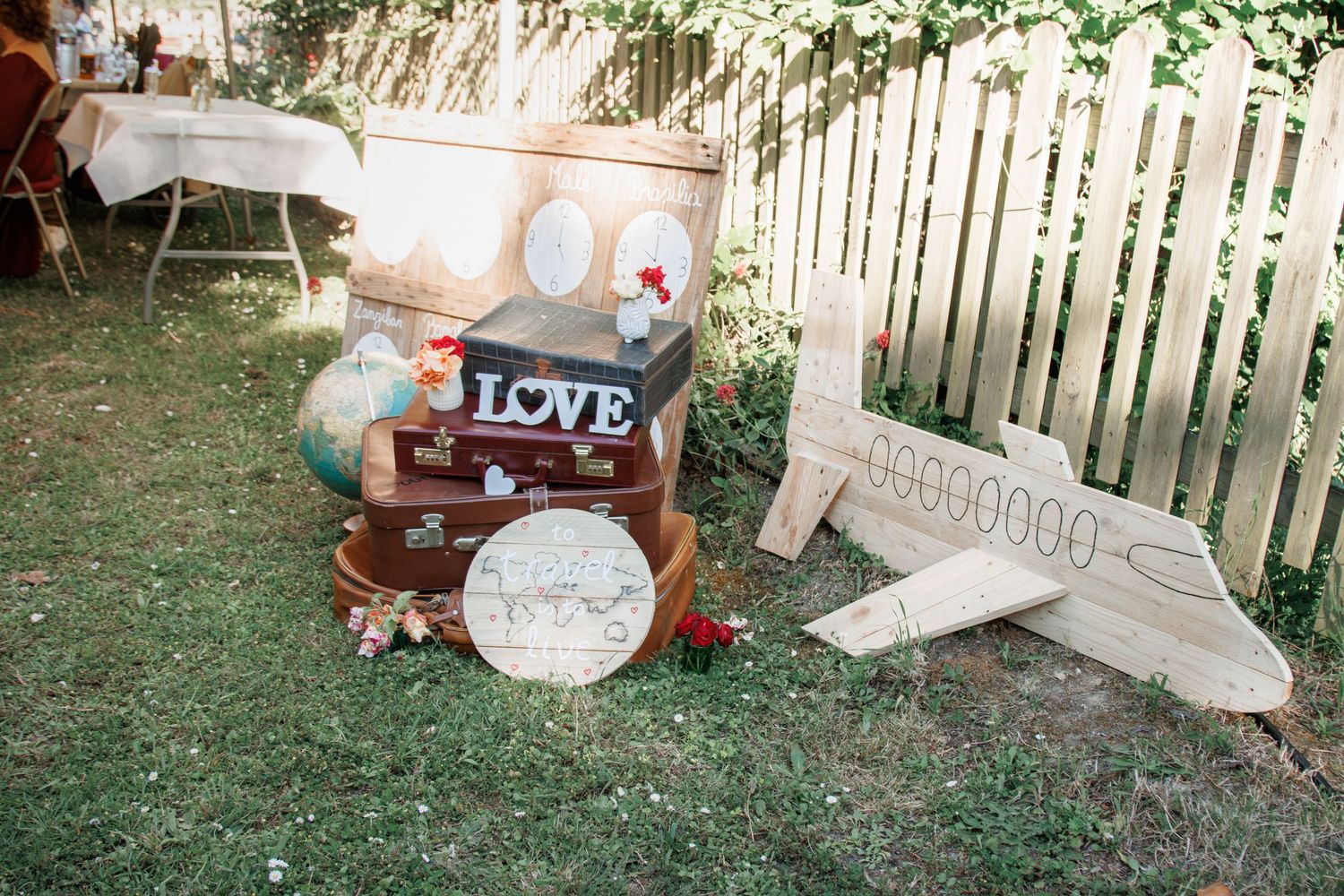 Vintage travel-themed wedding decor with globe, suitcases, and LOVE sign on garden lawn.
