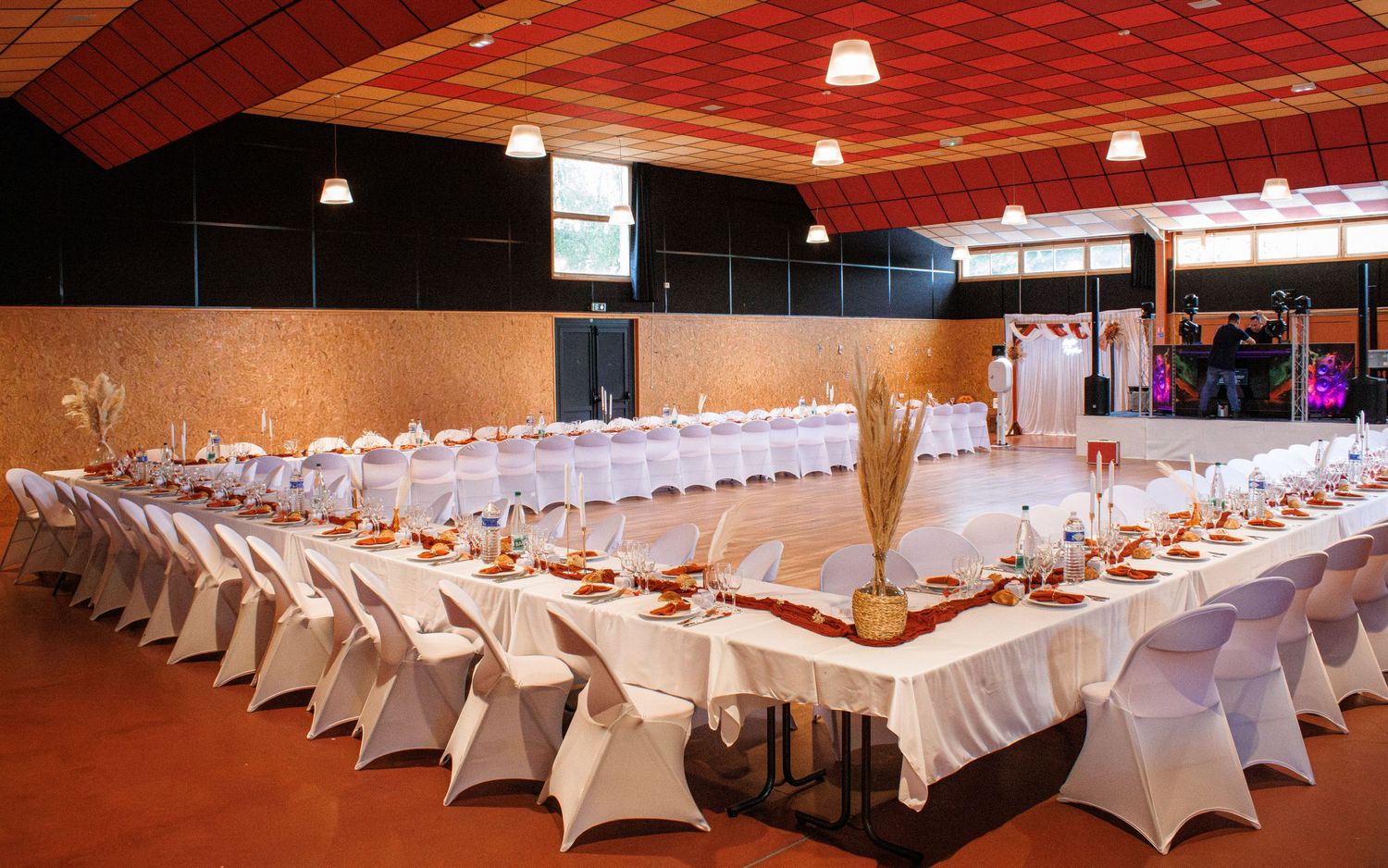 Elegant banquet hall with long tables, white chair covers, and red accents set for a formal event or wedding reception.