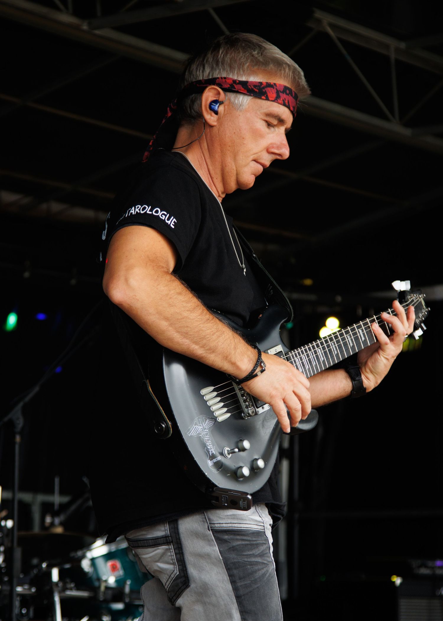 Musician playing silver guitar while performing on dark stage with colored lighting.