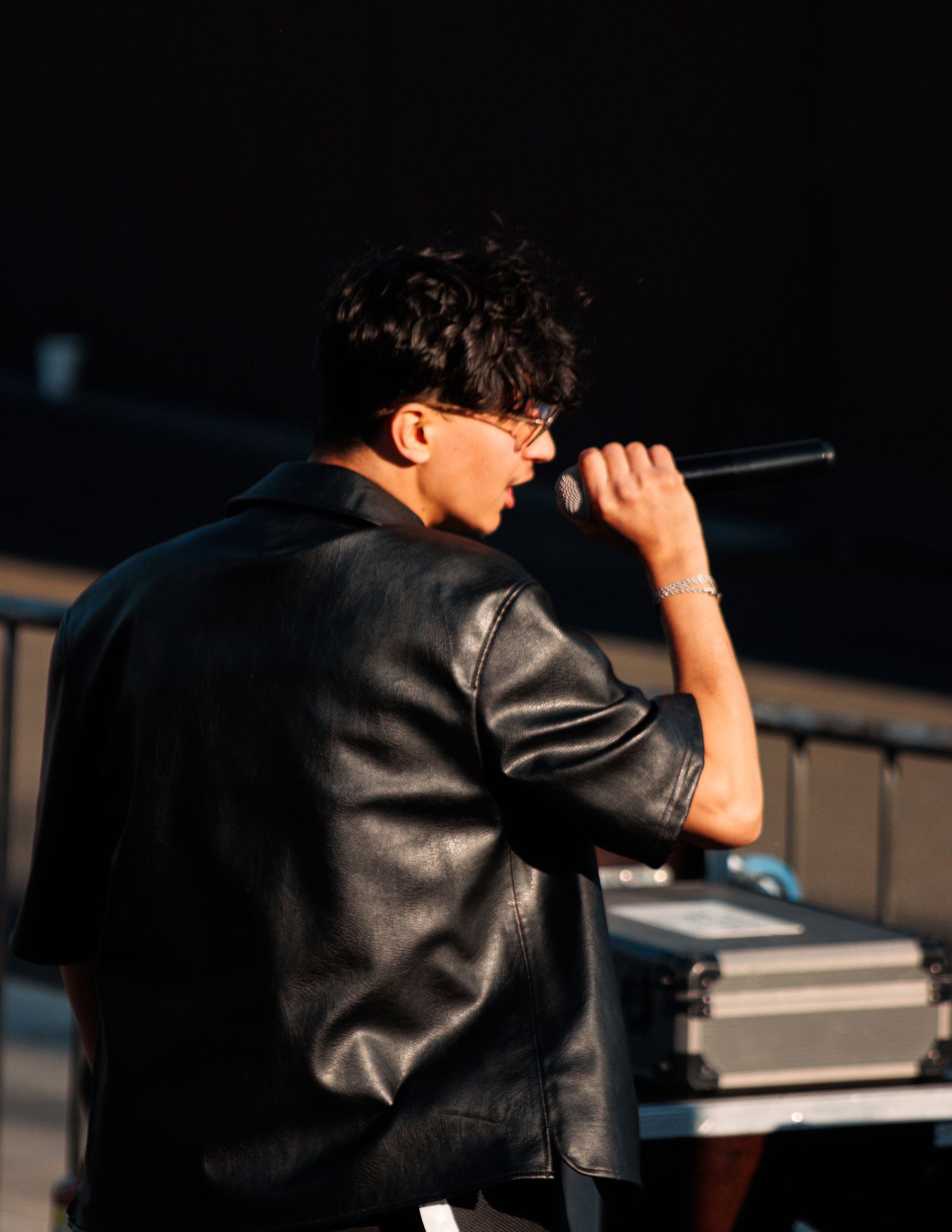 Side profile of performer in black jacket holding microphone on stage.