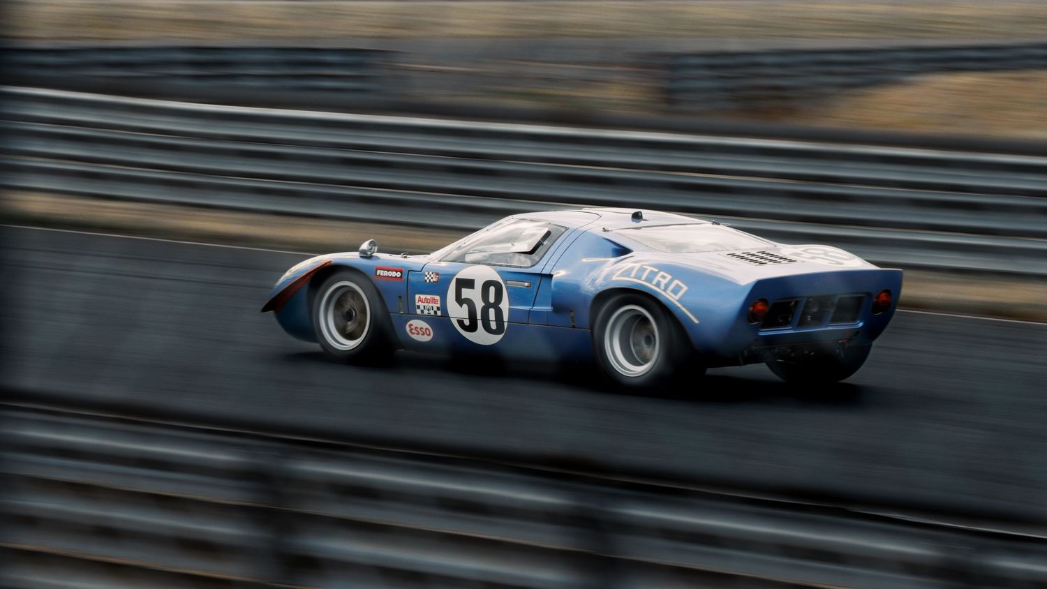 Vintage racing car in blue livery speeds around a racetrack curve during a motorsport competition.