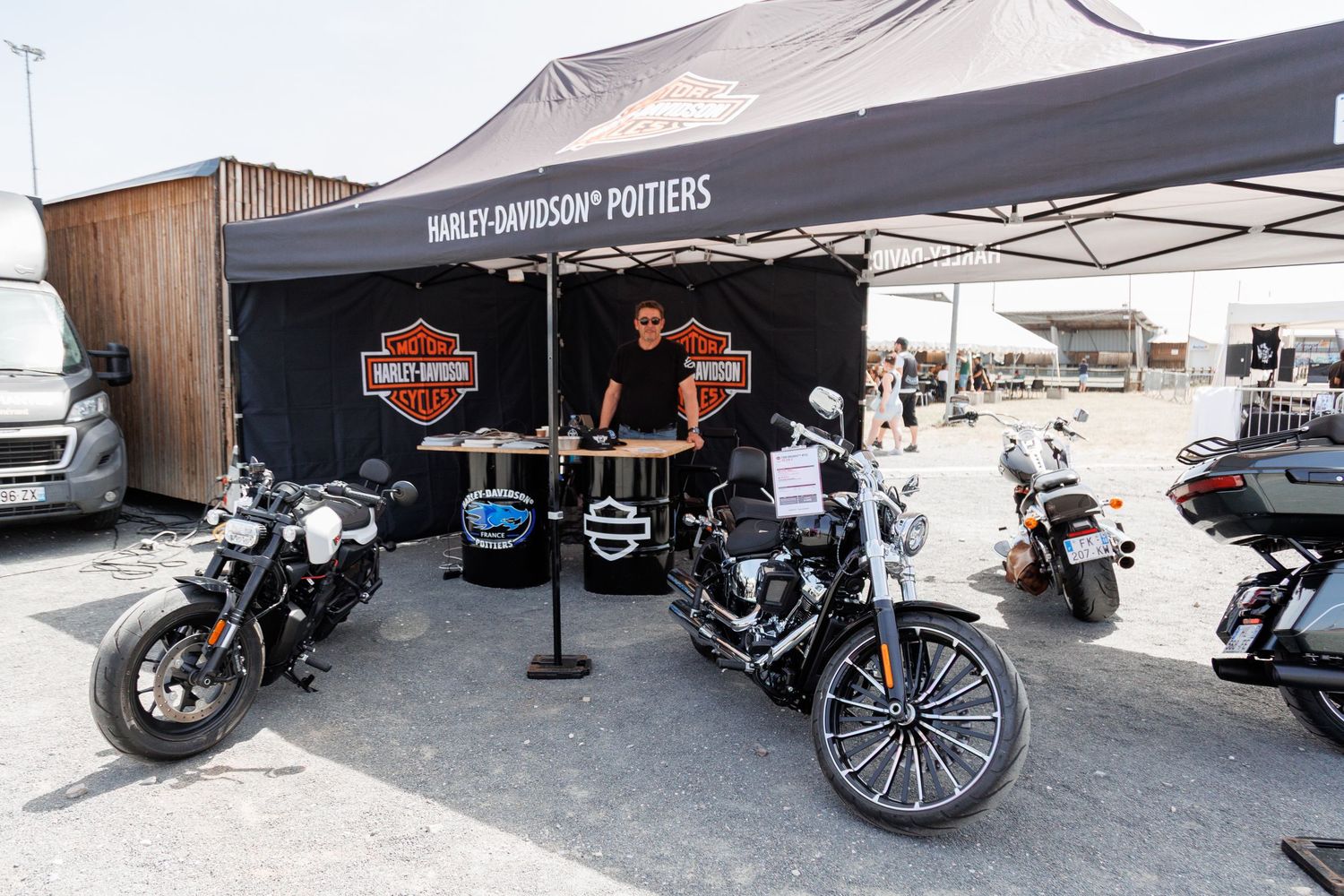 Harley-Davidson Poitiers booth with motorcycles displayed under a black tent at an outdoor motorcycle event.