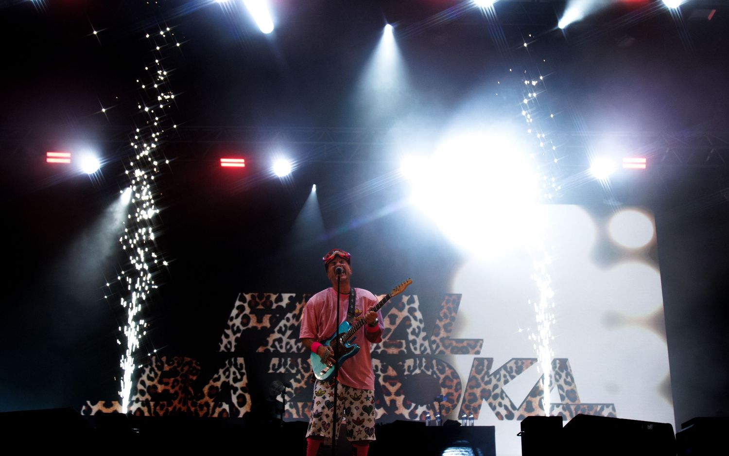 Concert stage lit with dramatic white spotlights and silhouetted performers creating an atmospheric live music scene.