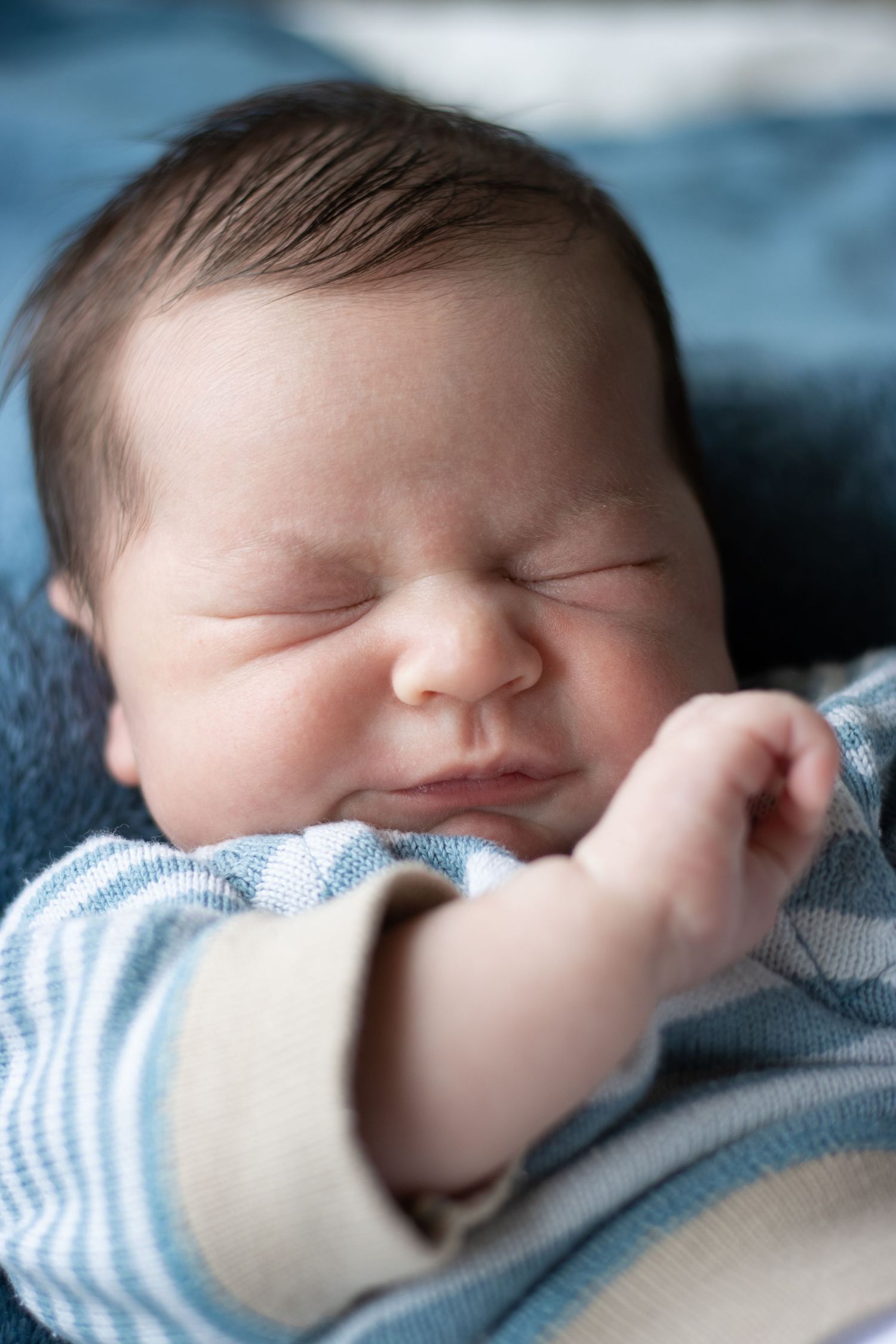 A peaceful sleeping newborn in striped clothing rests against blue textured fabric.